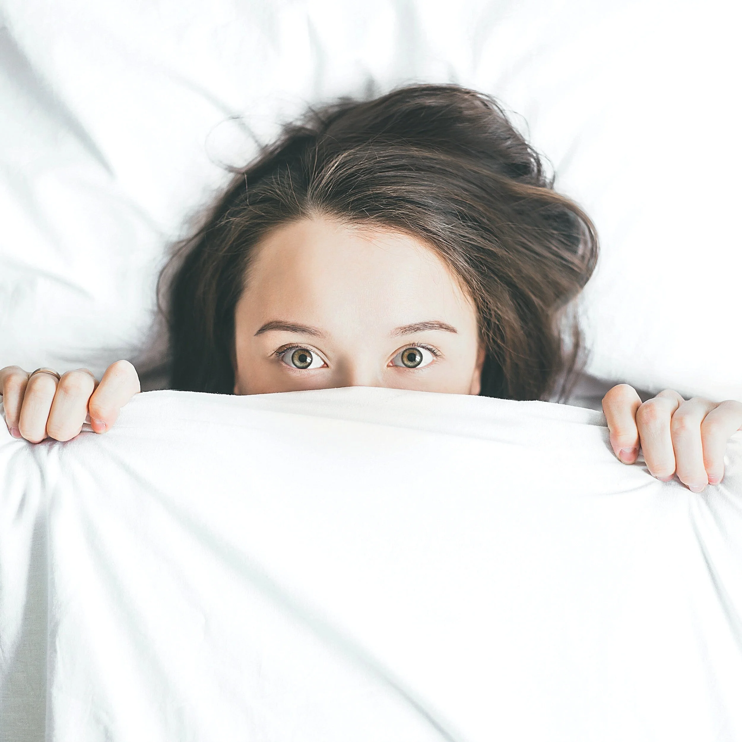 Young Woman peaking from behind bed sheet in mock fear