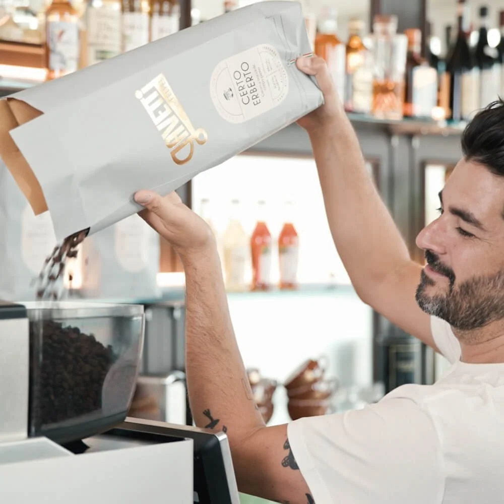An employee pouring coffee beans from a bag labeled 'Ceretto' into a grinder in a barista-level commercial coffee machine designed for corporate offices.