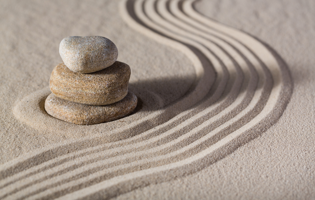 Three stacked pebbles on sand with patterned lines in the background to represent peace and tranquility.