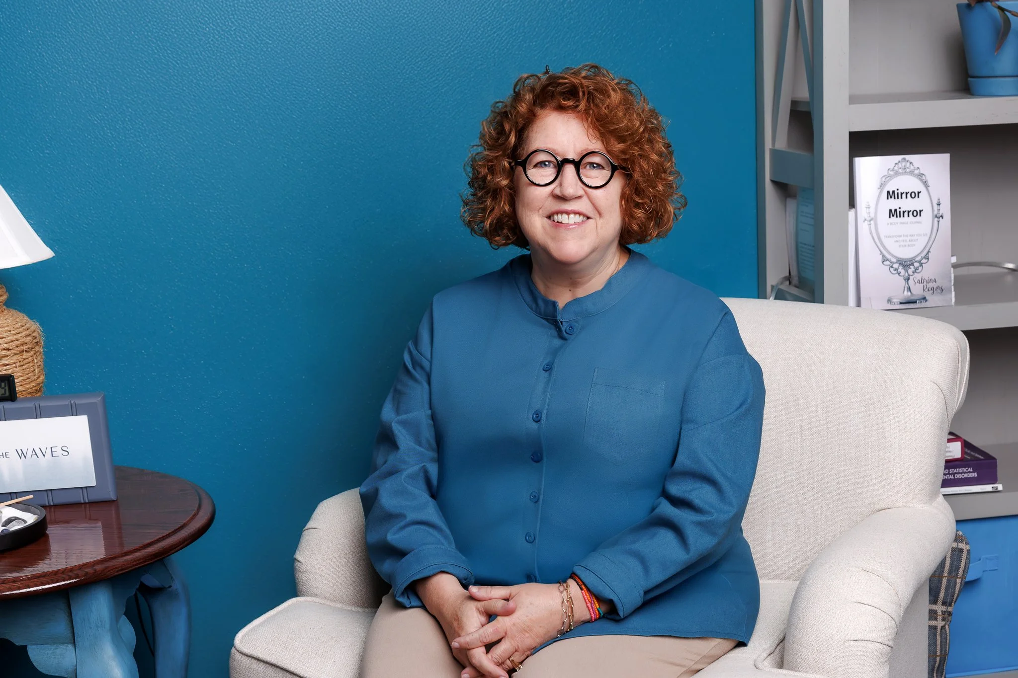 Naomi with curly hair and round glasses smiling against a plain backdrop.
