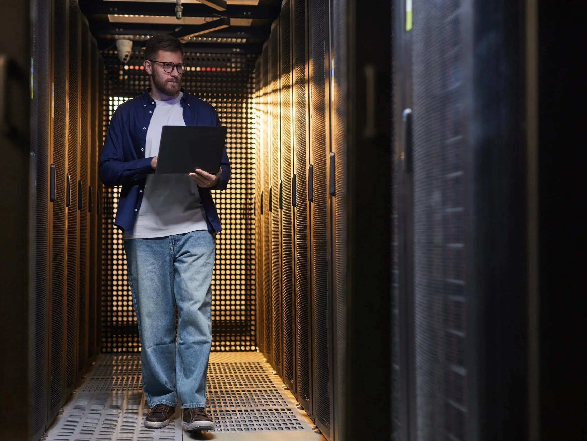 Engineer with a laptop working between server racks in a data center aisle.