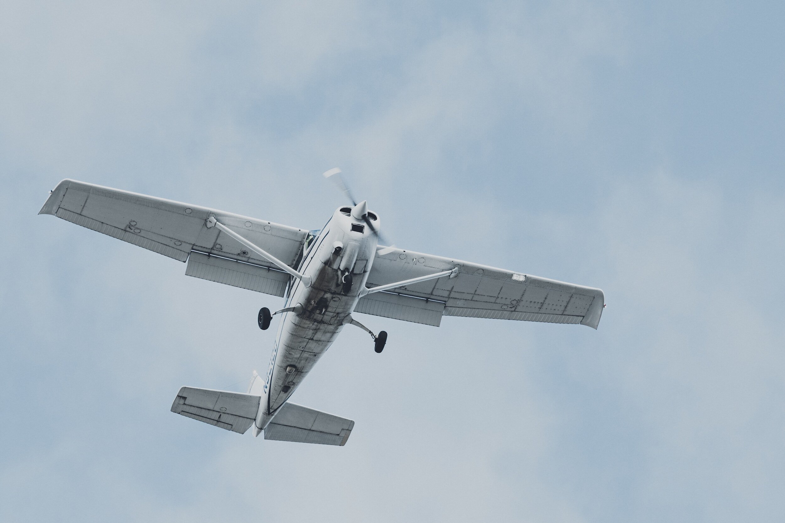 A white single-engine airplane flying in the sky viewed from below.