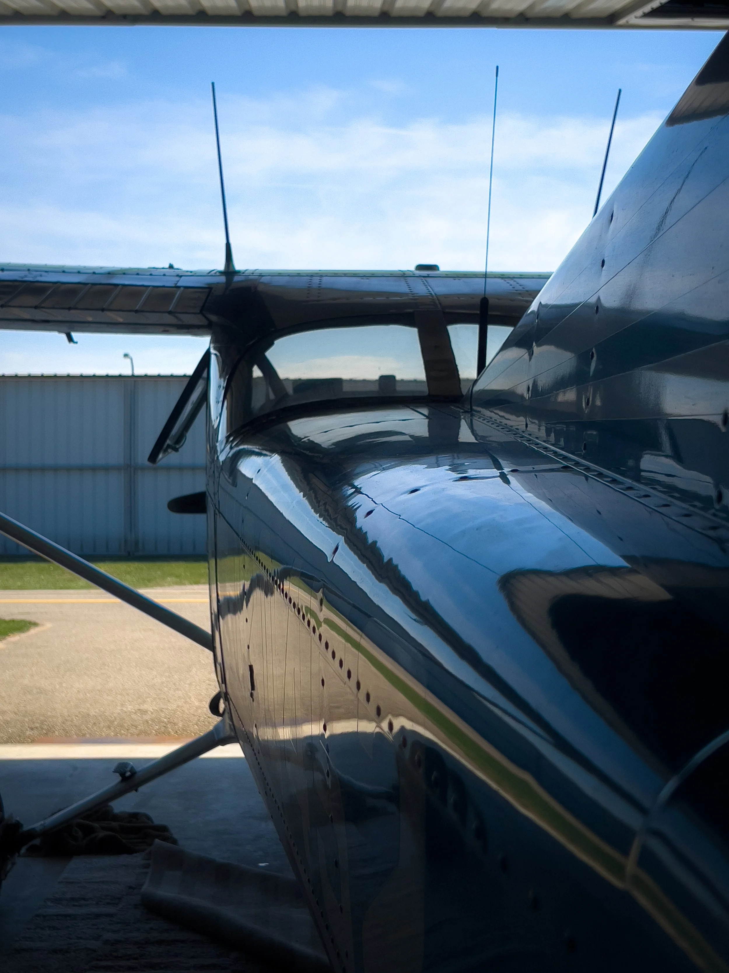 The image shows a side view of a small airplane parked in a hangar, with its nose and wing visible, reflecting sunlight