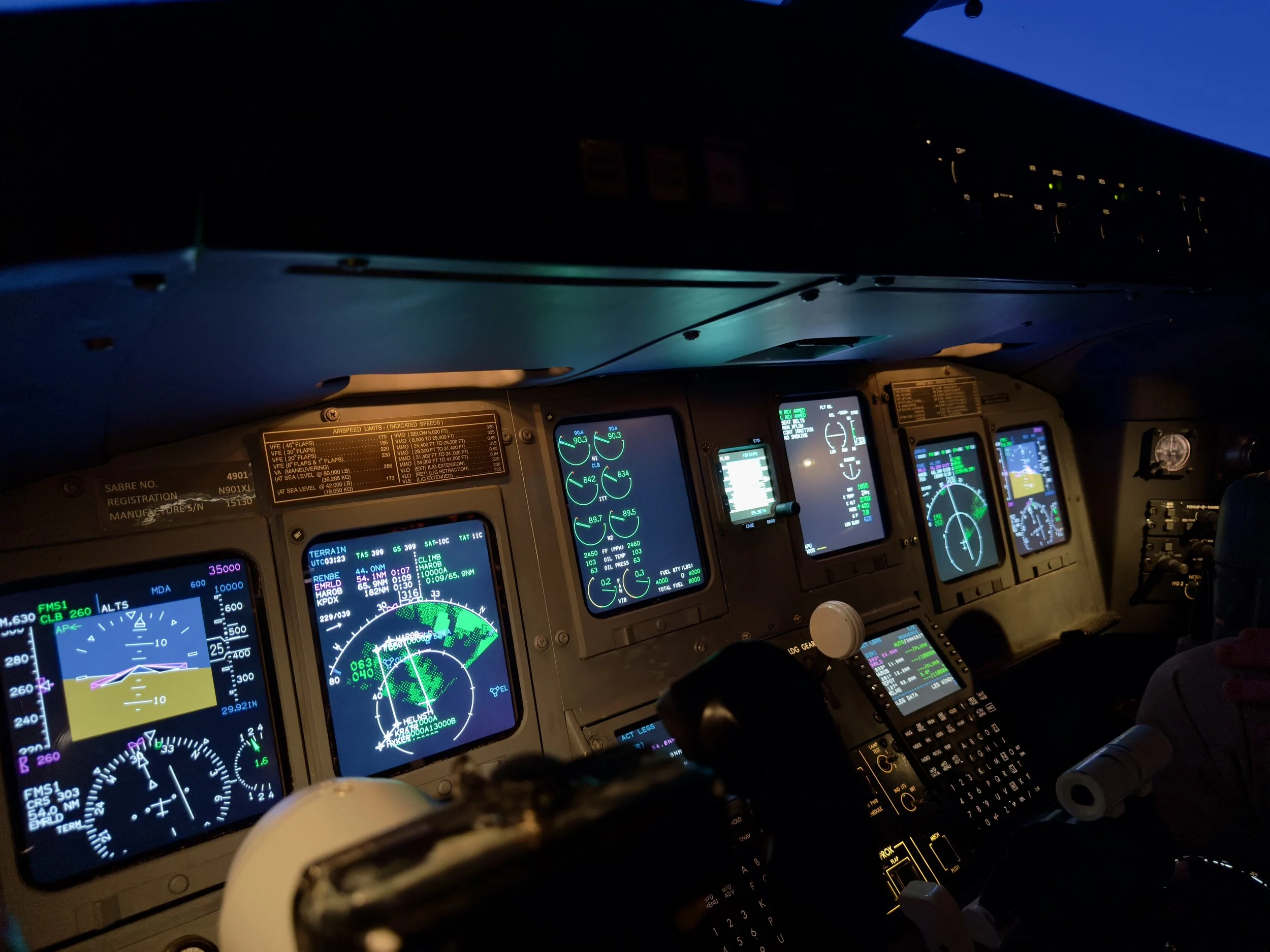 Photo of an airplane cockpit at night with illuminated instrument panels and screens showing navigational and system data.