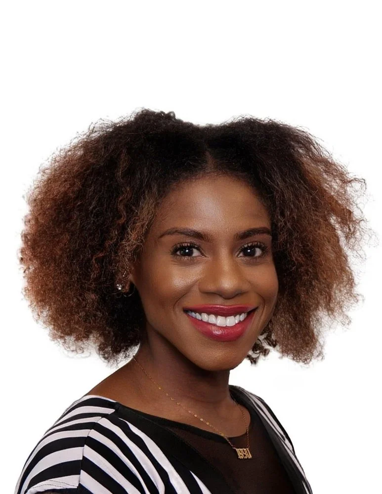 Portrait of a woman with curly hair, wearing a black and white striped shirt, smiling against a white background.