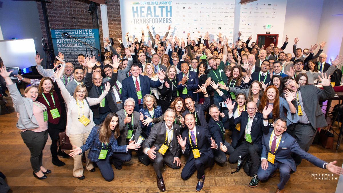A room full of Health Transformers with their arms in the air at a StartUp Health gathering