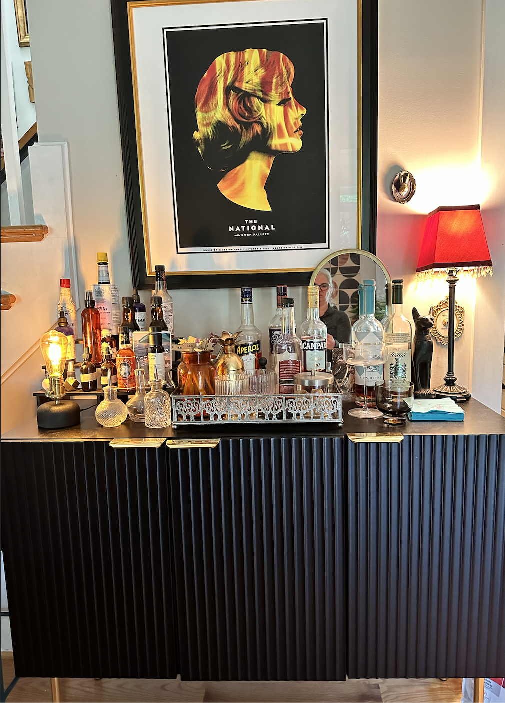 DETAIL: The gorgeous bar - again, a rich textured black cabinet, this time with brass handles and legs, but adorned with numerous older-vintage finds, like the ornate metal mirrored tray the bottles rest on, and the Edison bulb at left, plus the bead