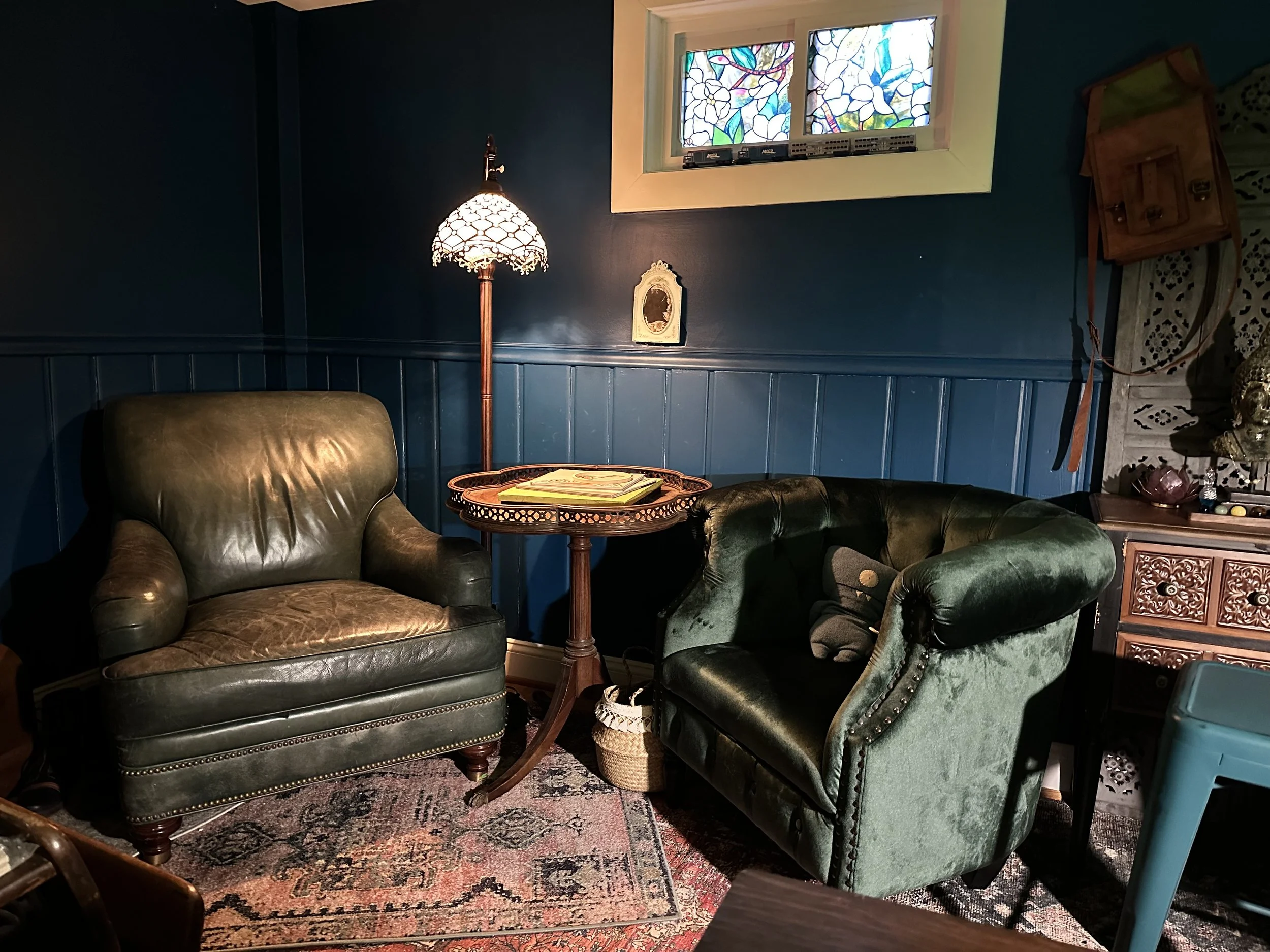 AFTER: various thrifted rugs overlapping create a cozy pallet of jewel tones to go with the moody deep teal paint. The green leather stuffed chair and clover accent table are actual antiques (from a curbside find and an estate sake, respectively), an