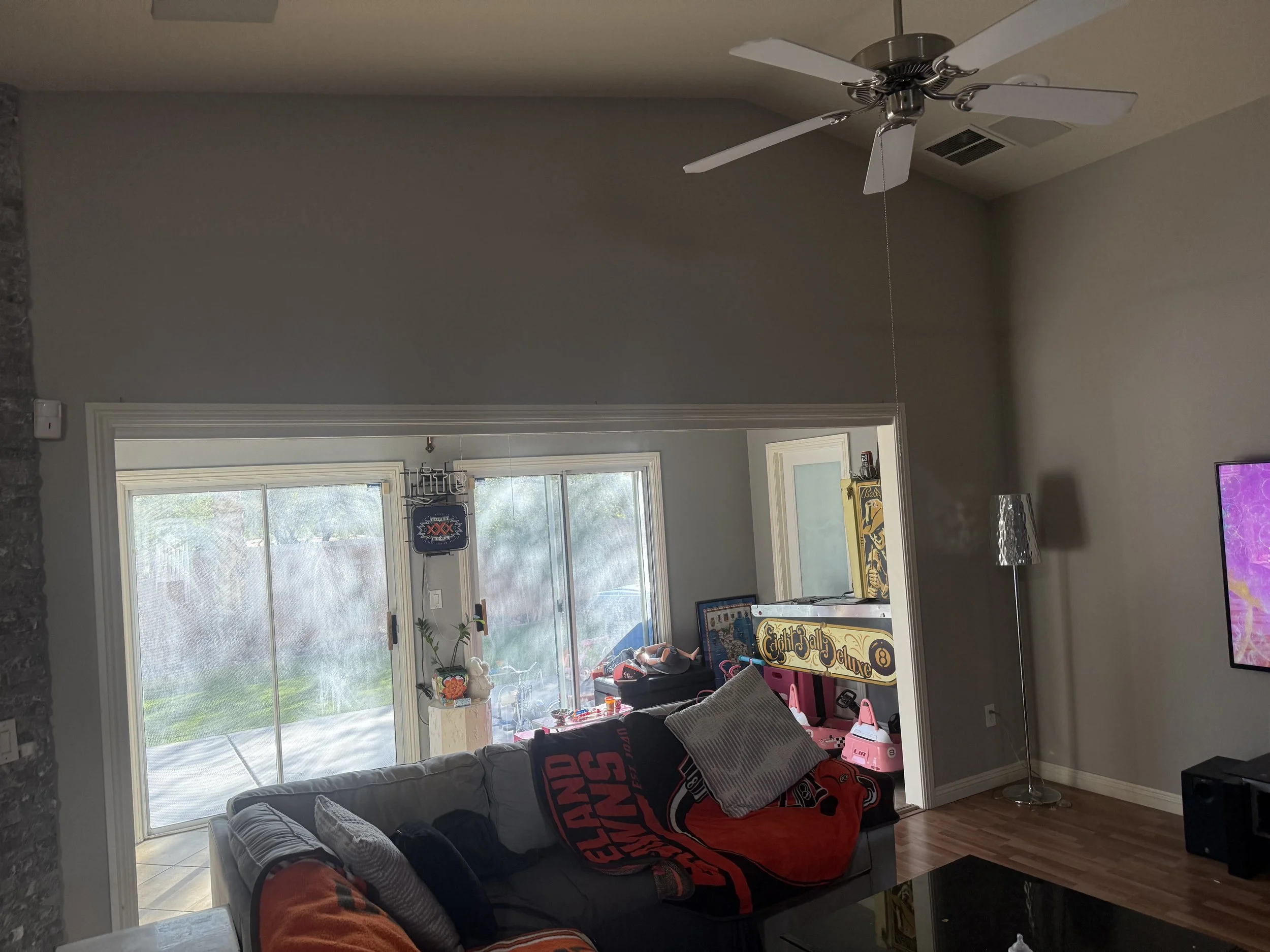 A living room with a ceiling fan, a gray sofa with black, white, and red blankets, and a sliding glass door leading to an outdoor area.