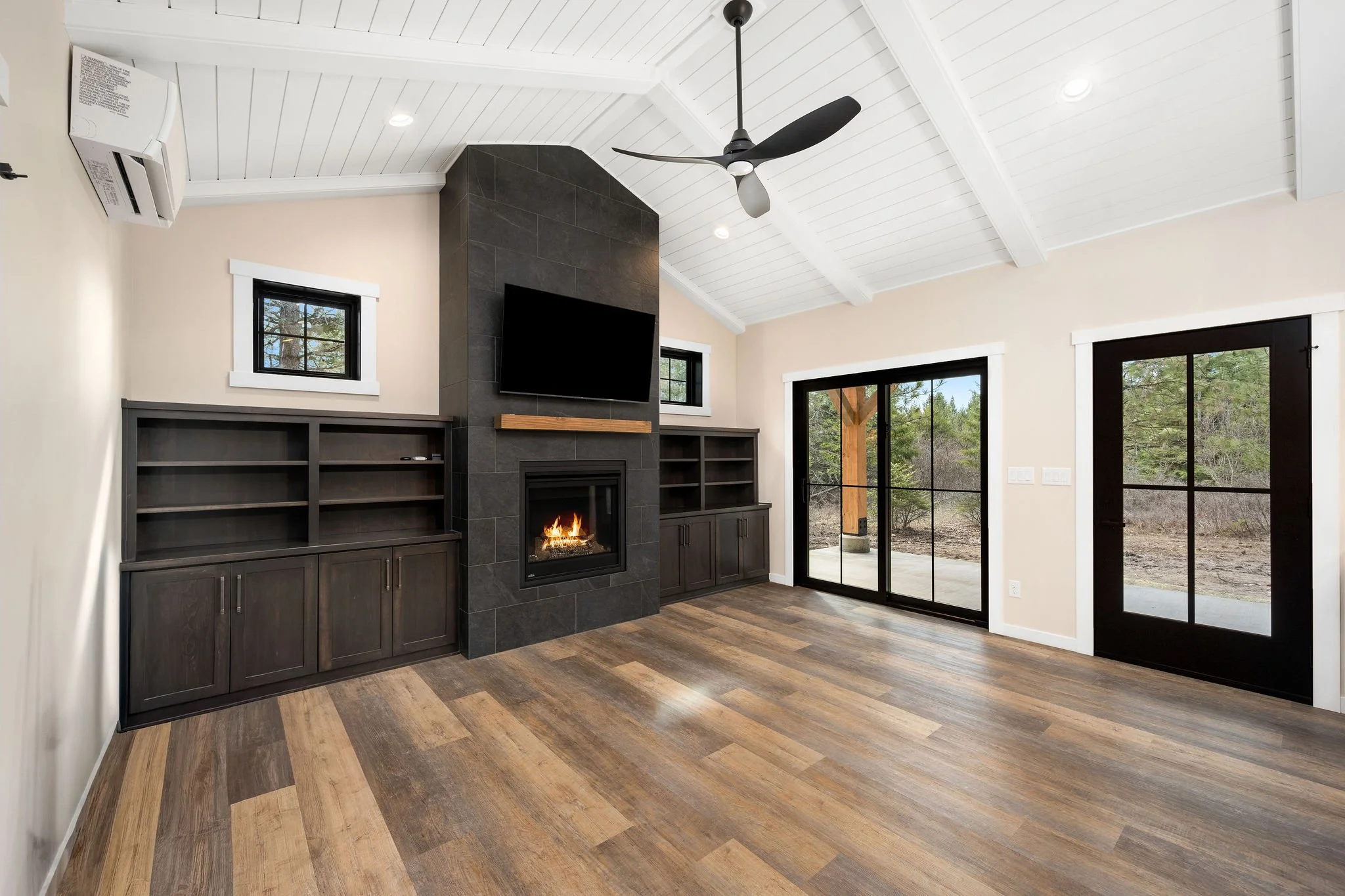 A custom Coeur D'Alene ADU living room with wood flooring, a fireplace, built-in bookshelves, large sliding glass door, windows, and a ceiling fan.