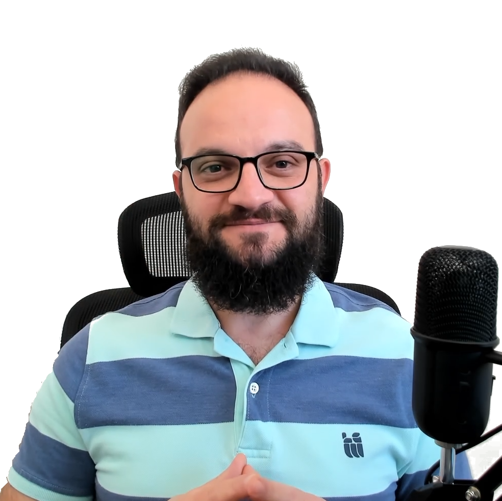 Man with glasses and beard sitting in front of microphone, smiling, wearing a light blue and dark blue striped polo shirt, in a home studio or office environment.