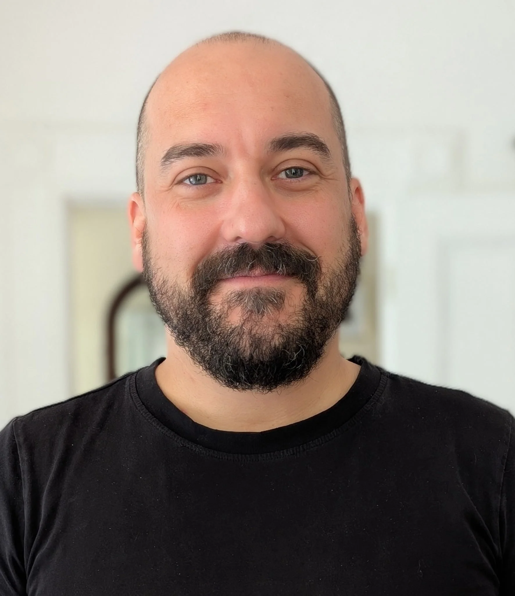 Man with a beard and mustache, wearing a black t-shirt, smiling lightly