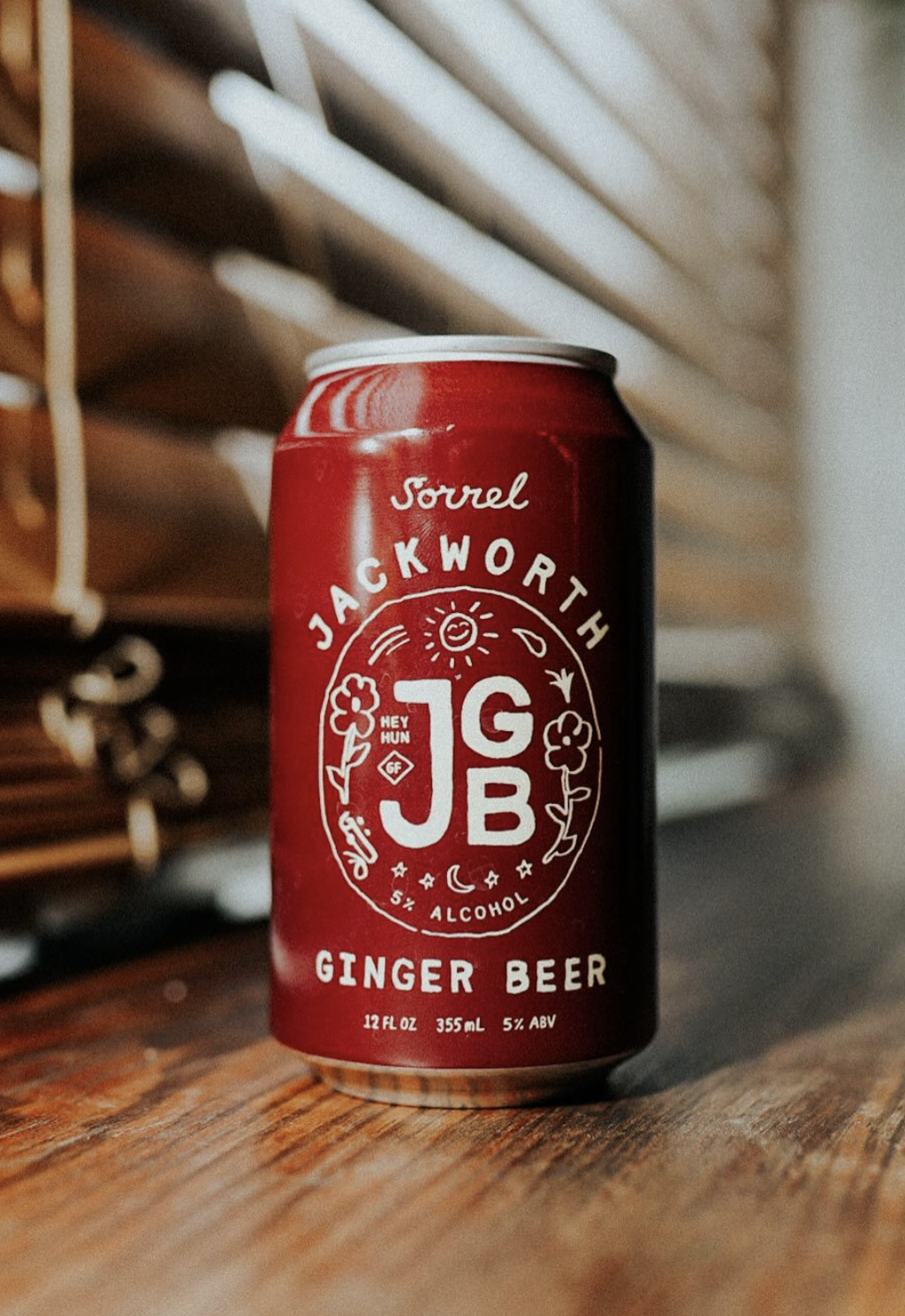 Red can of Jackworth Ginger Beer with 5% alcohol, 12 oz, placed on a wooden surface, with a blurred background of wooden slats.