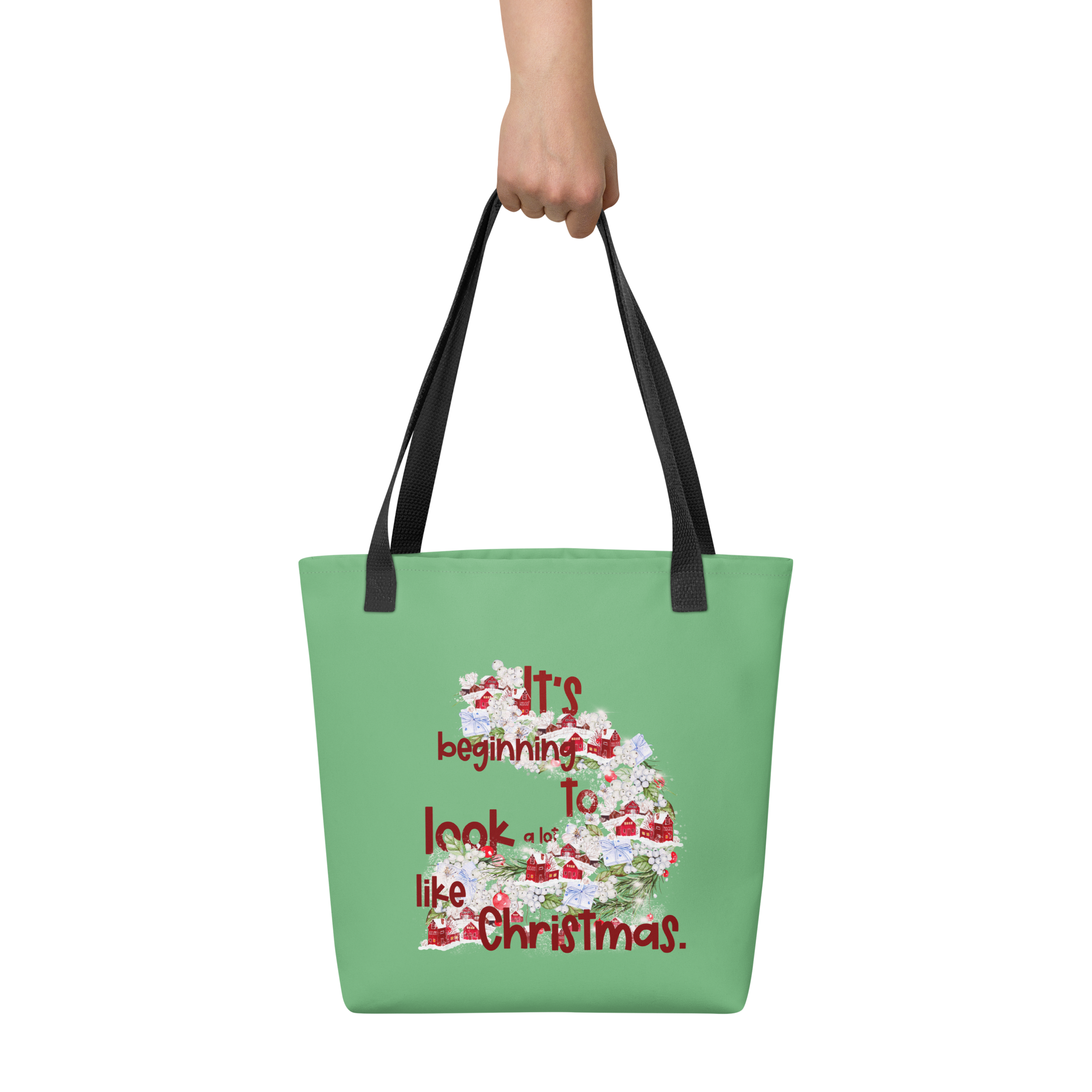 Image of a hand holding a green tote bag with a black handle that has a festive design and the words It's beginning to look a lot like Christmas.