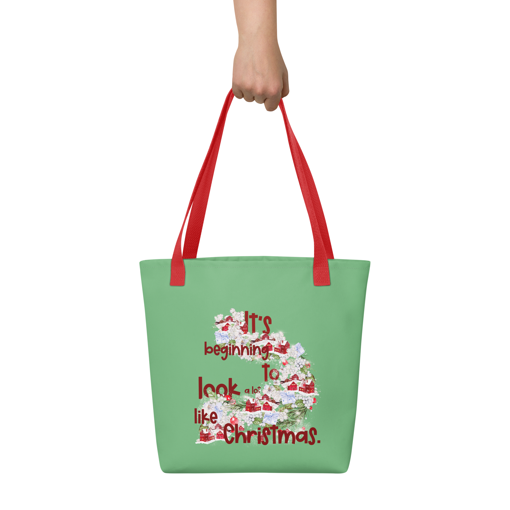 Image of a hand holding a green tote bag with a red handle that has a festive design and the words It's beginning to look a lot like Christmas.