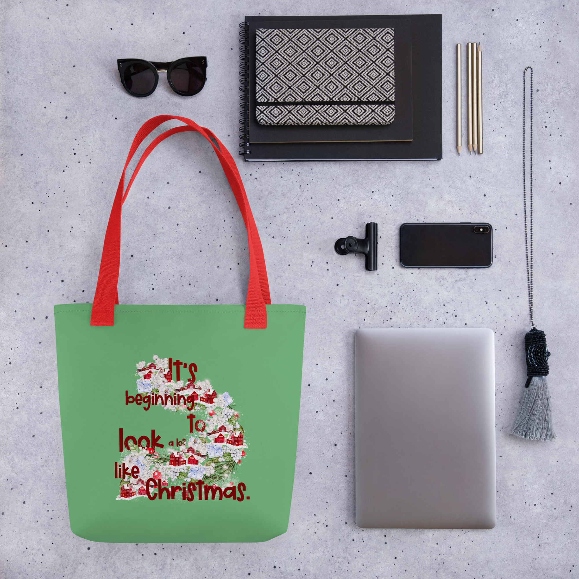 Lifestyle photo of a green tote bag with a red handle that has a festive design and the words It's beginning to look a lot like Christmas.