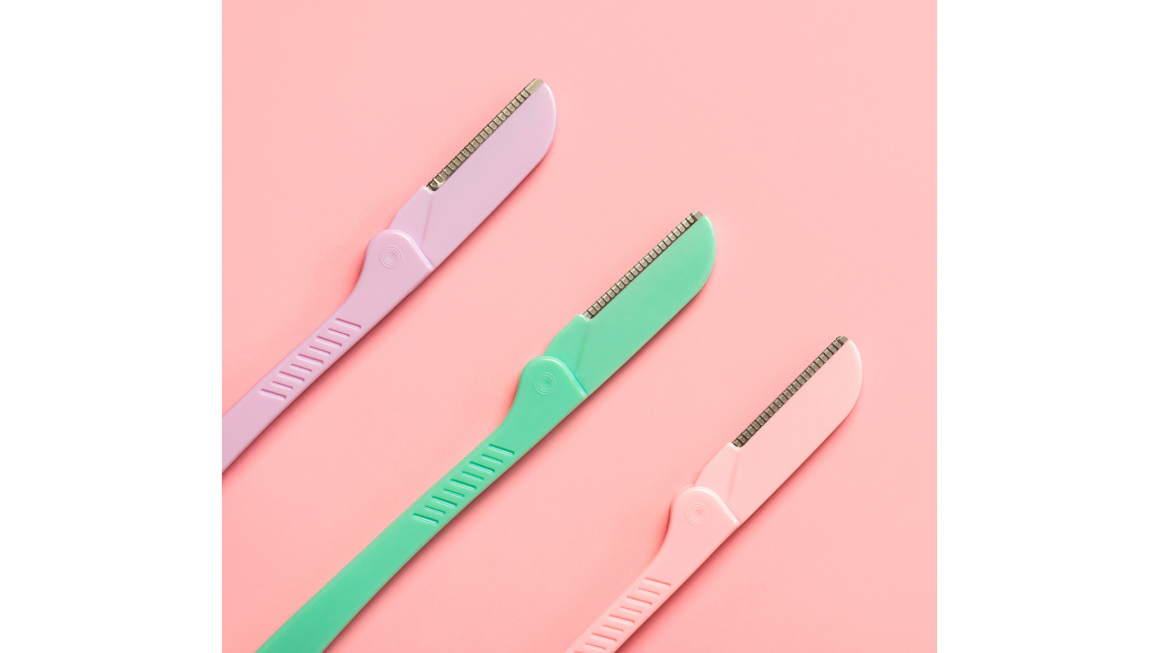 Three rows of disposable dermaplane razors in pink, green, and pastel pink colors on a pink background.