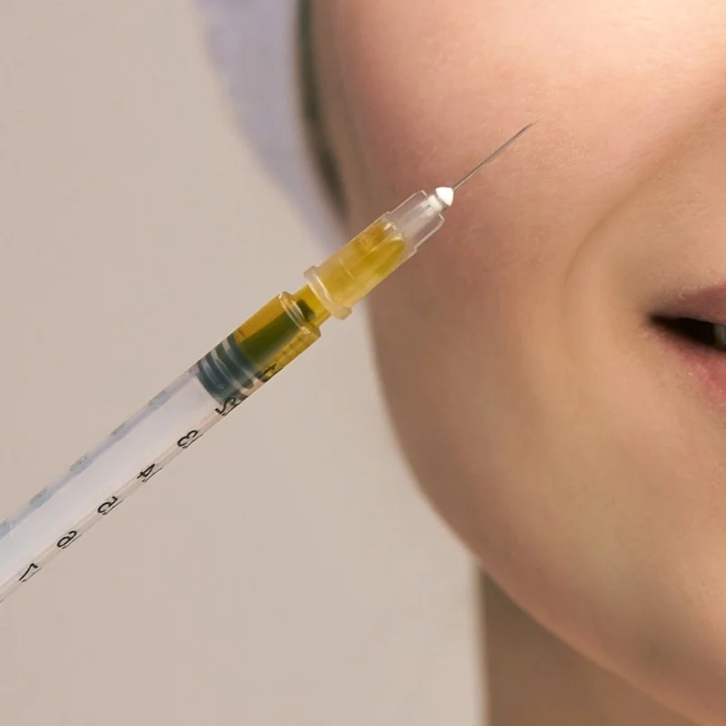 Close-up of a person receiving a cosmetic injection in their cheek with a syringe.