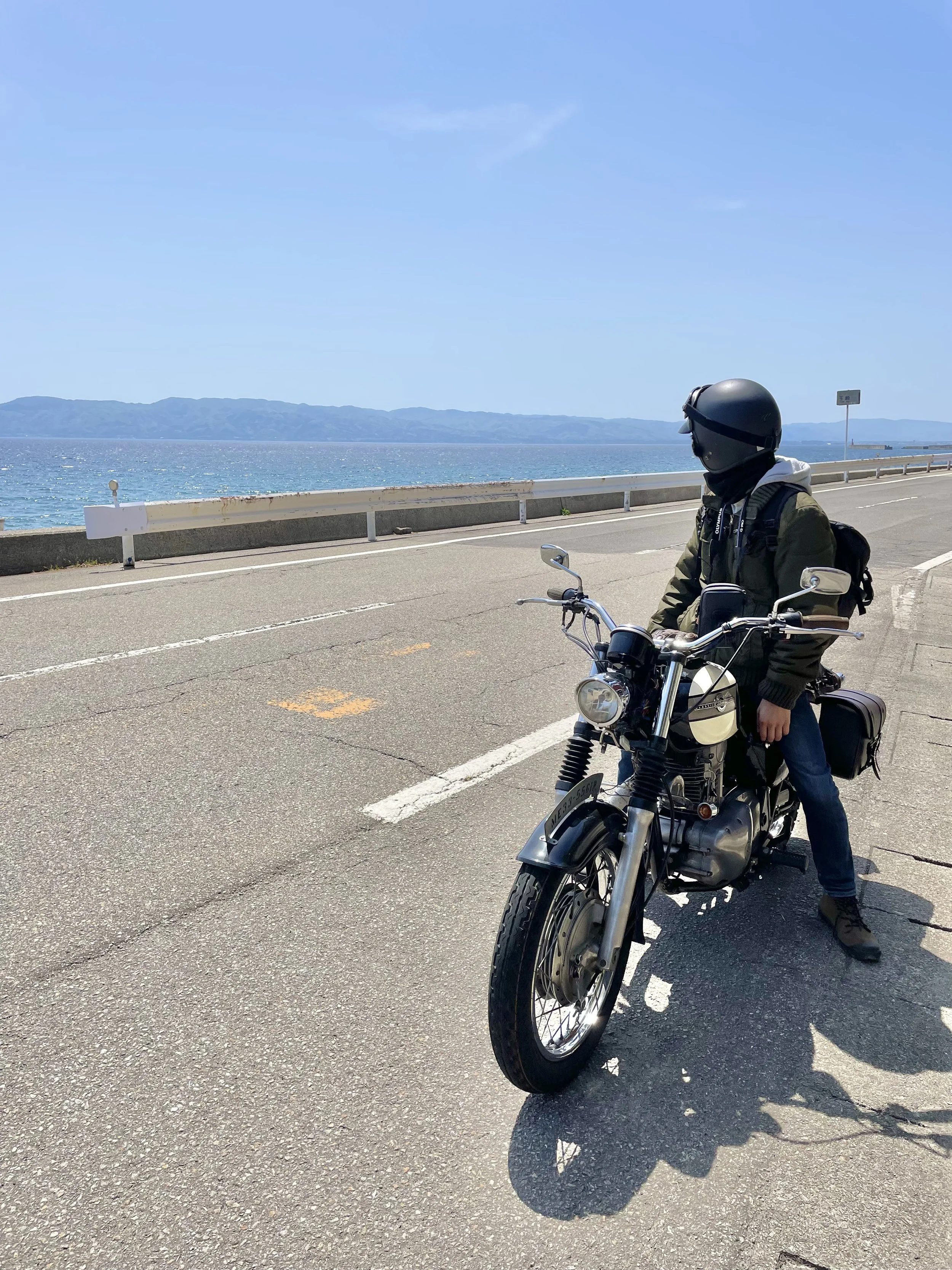 A person wearing a helmet sits on a motorcycle parked on a coastal road with an ocean view.