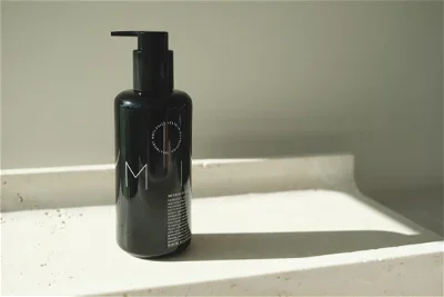 A black pump bottle on a white surface, with a faucet and sink in the background.