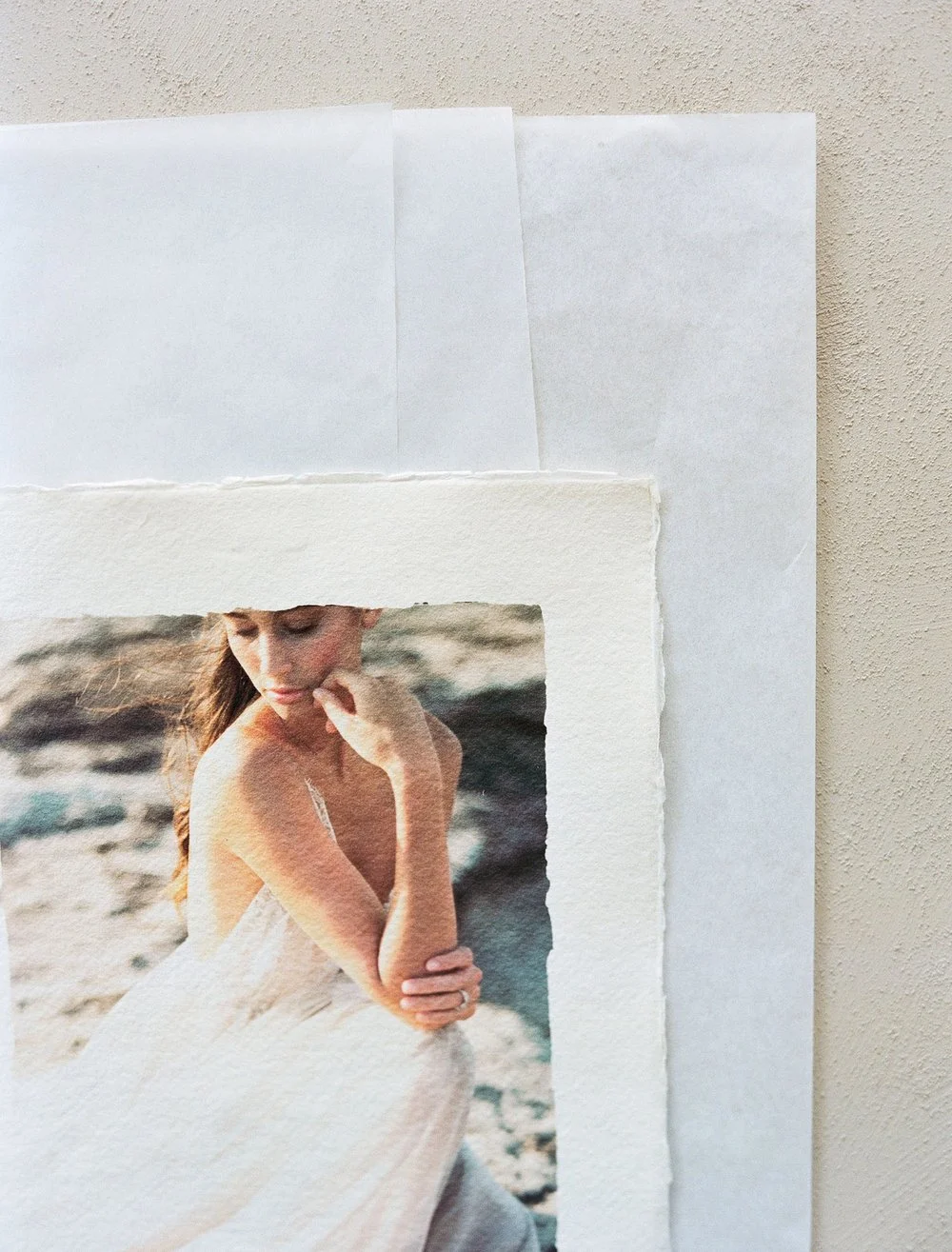 Artistic photograph of a person in a light-colored dress with a thoughtful pose on textured paper.