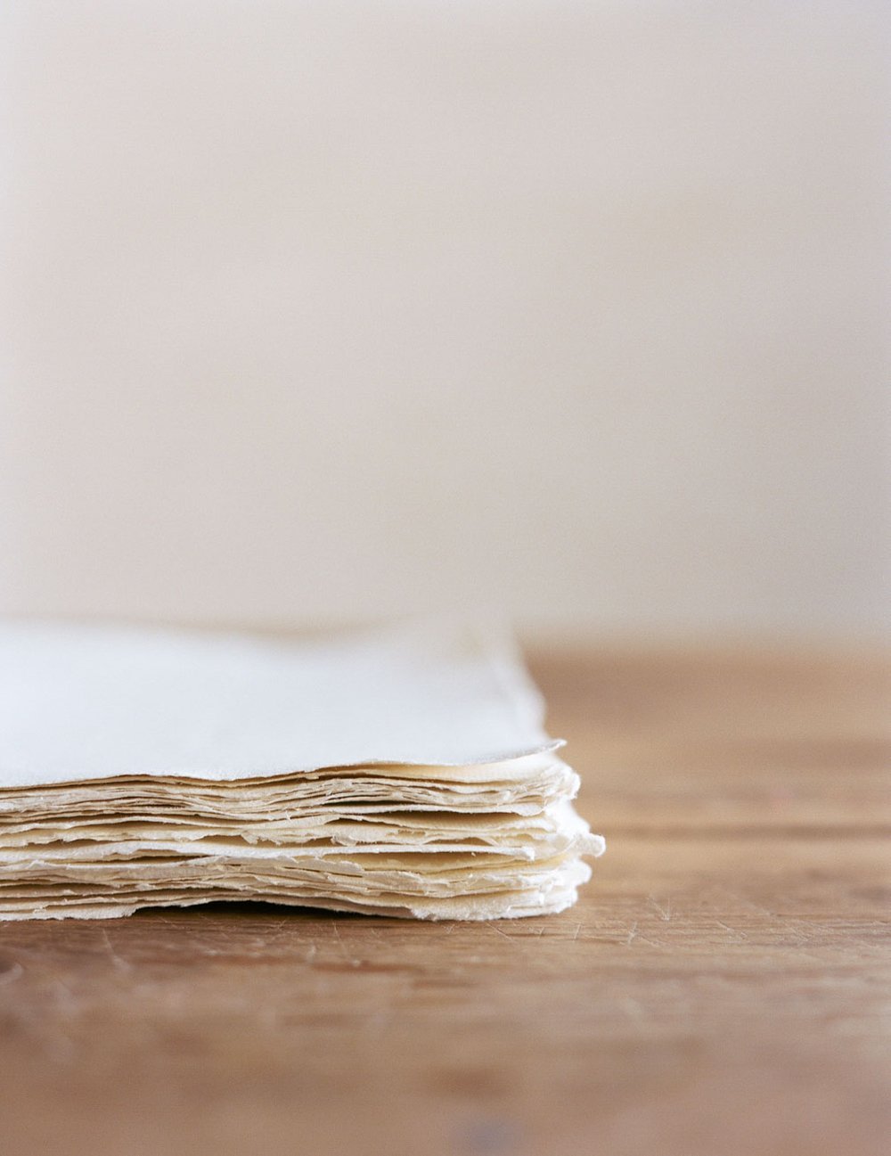 A stack of textured, off-white paper sheets on a wooden surface.