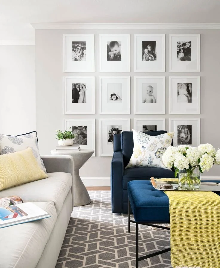 Living room with gallery wall, white sofa, blue armchair, side table, vase of flowers, and decorative pillows.