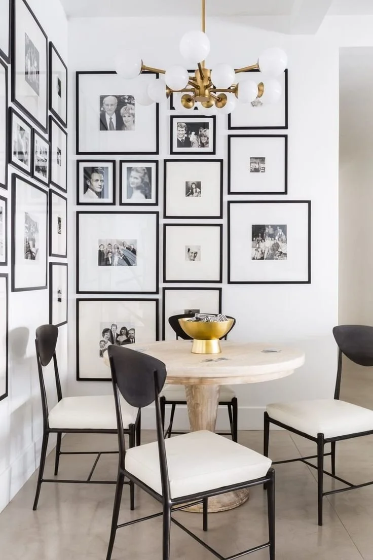Dining area with round table, black chairs, wall of black-and-white photos, modern chandelier, and decorative bowl.