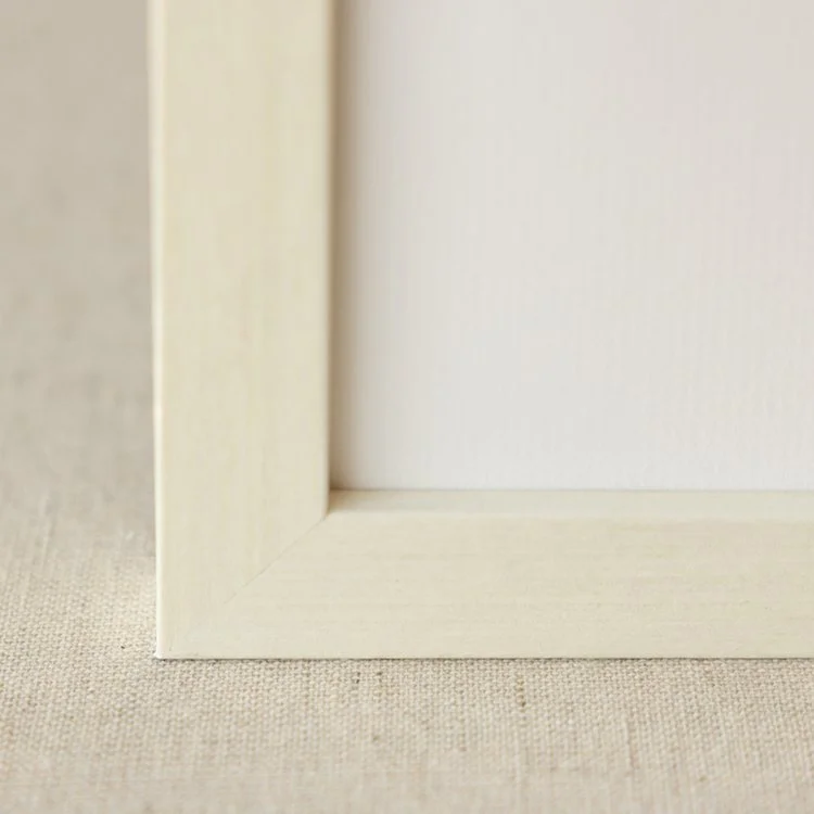 Close-up of a light-colored wooden picture frame corner on a textured beige surface.