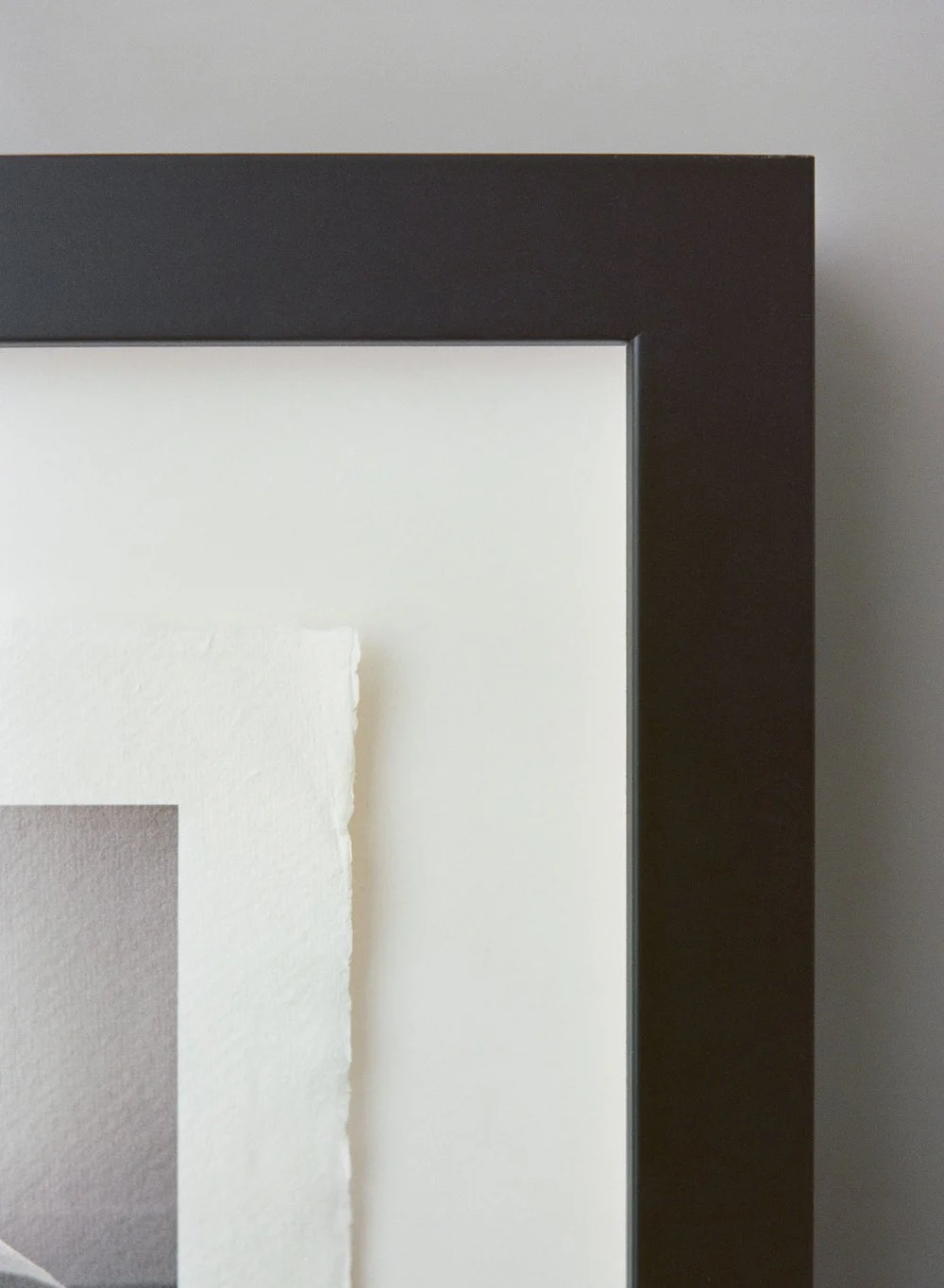 Close-up of a black picture frame corner with a textured white mat board.