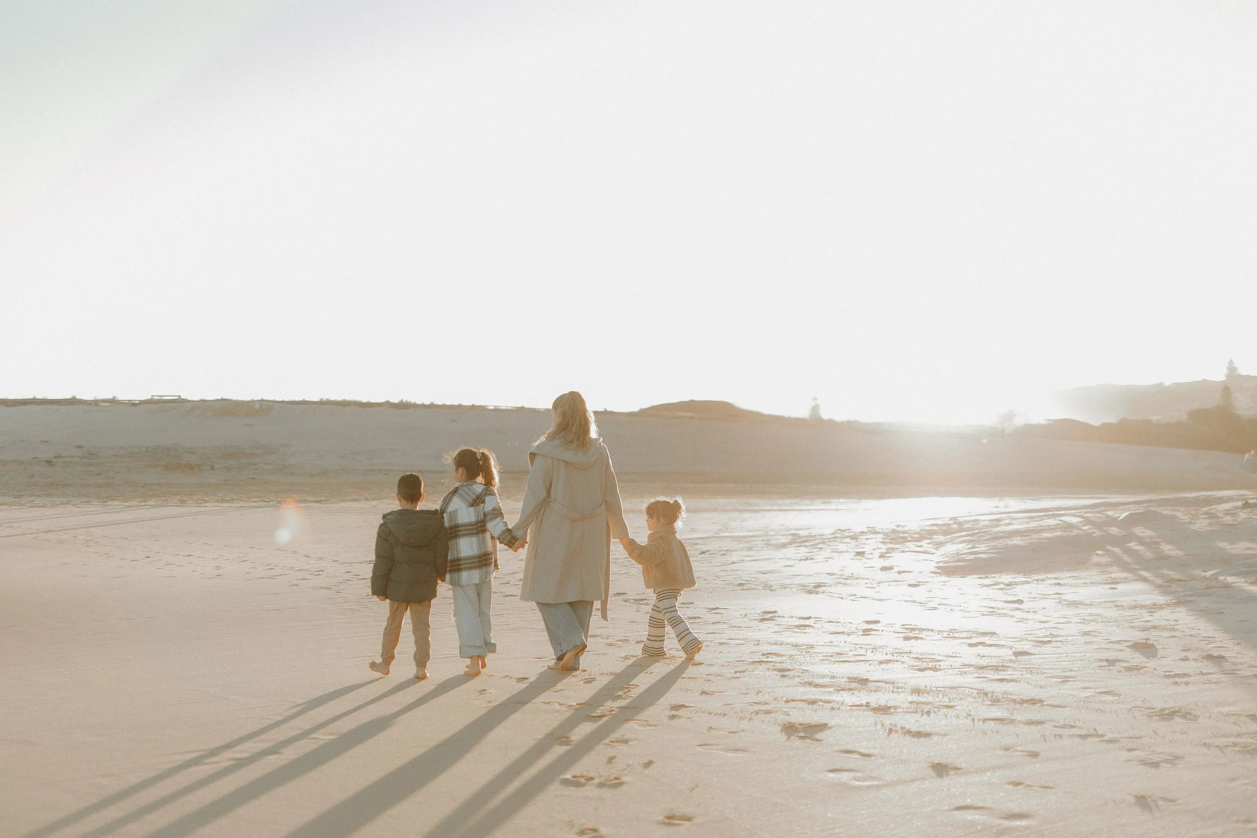 A group of five people walking on the beach during sunset, holding hands, with their shadows stretching on the sand.