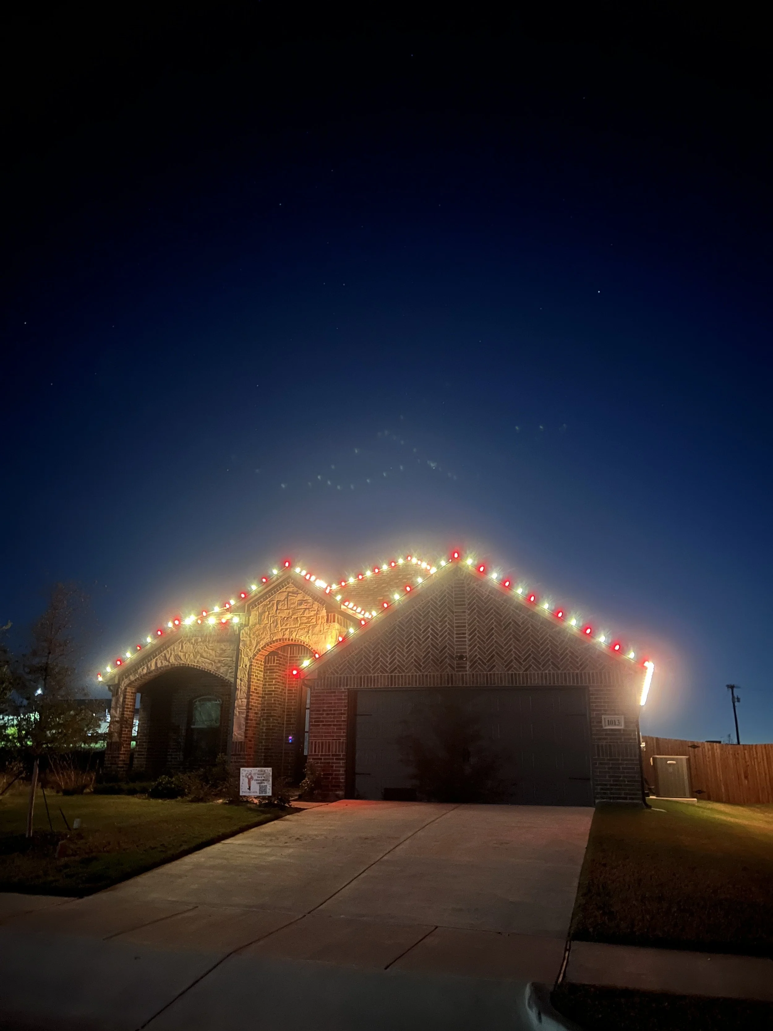 A house decorated with Christmas lights along the roofline at night, with a dark clear sky overhead.