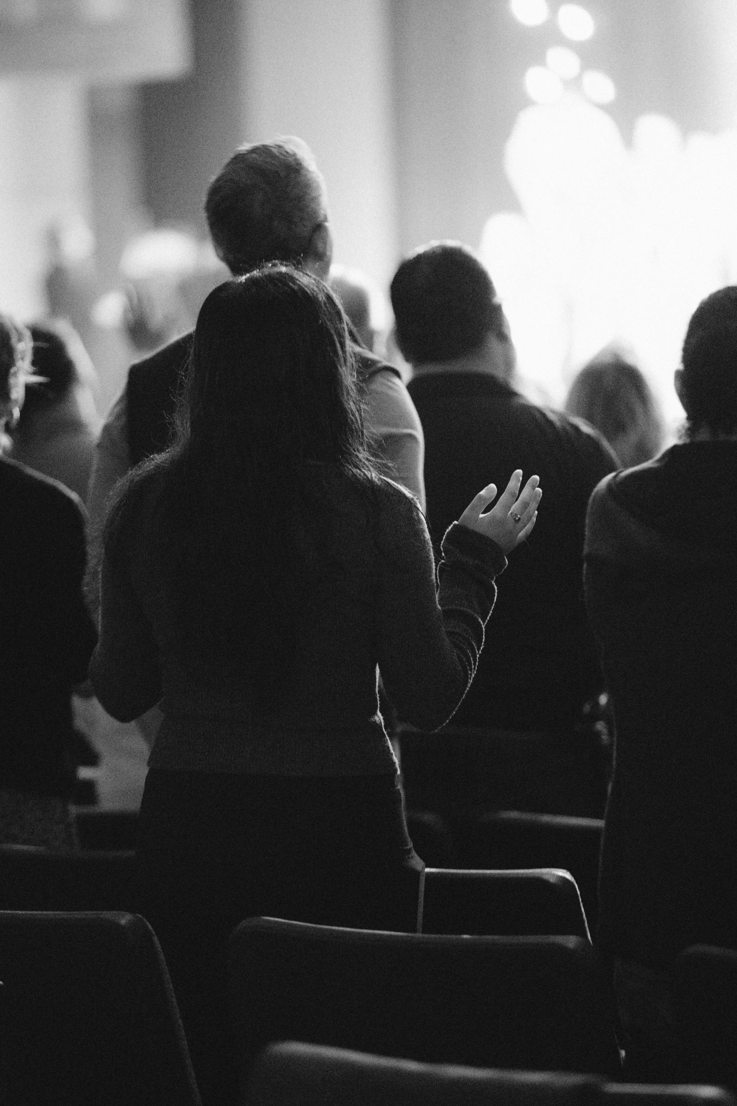Black and white photo of people sitting in an audience at a conference, with one woman standing and raising her hand.