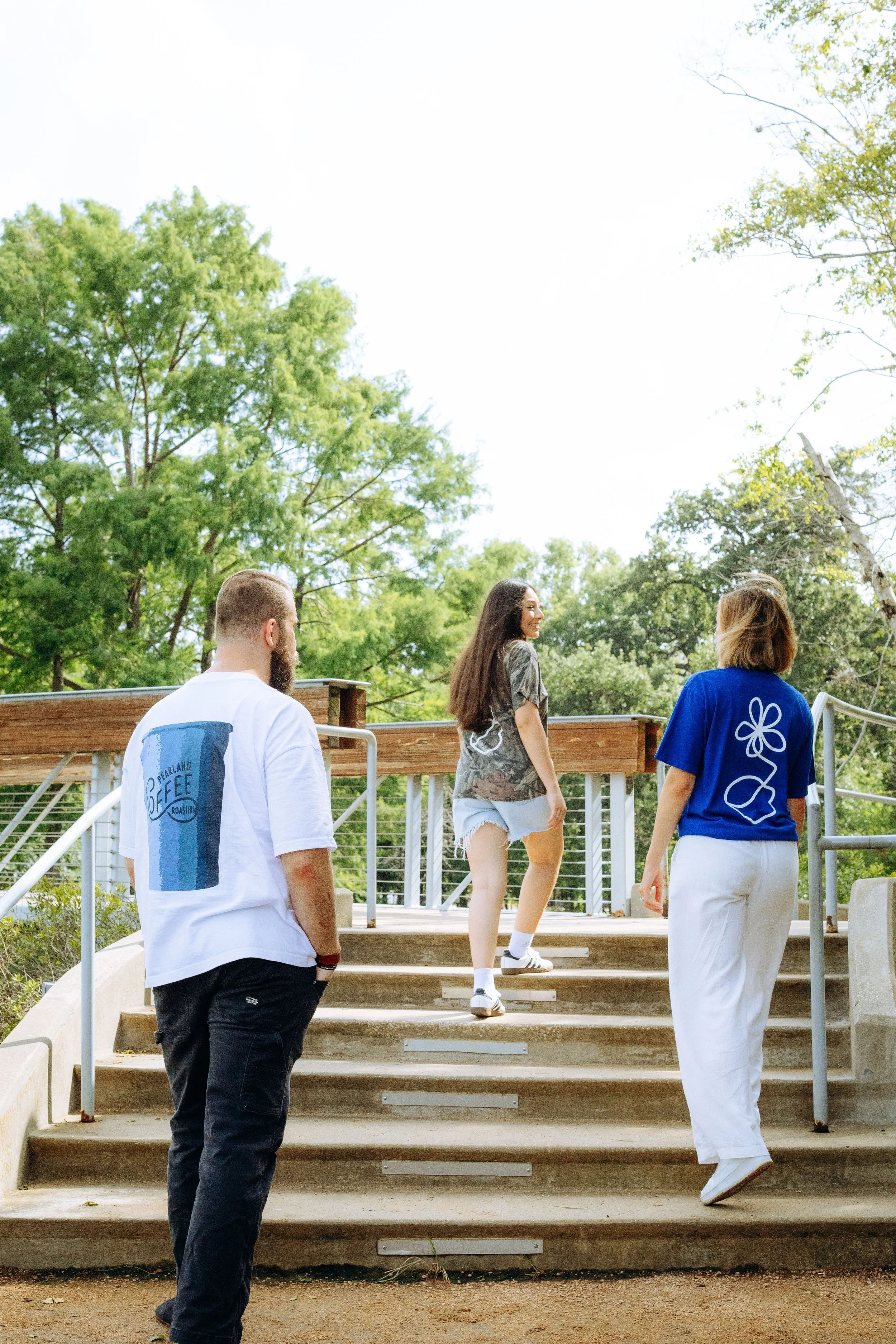Three people walking up outdoor stairs with green trees in the background.