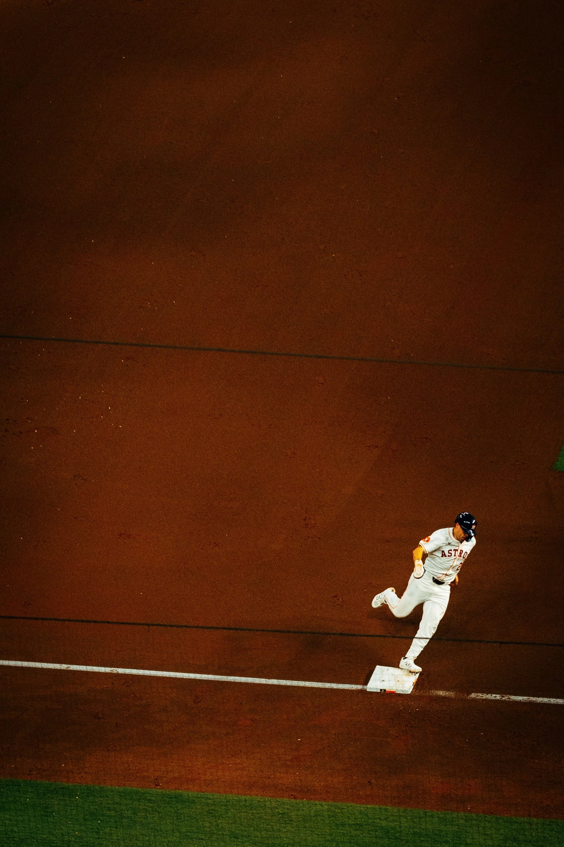 A baseball player in a white uniform with 'Astros' written on it runs past second base on a baseball field at night.