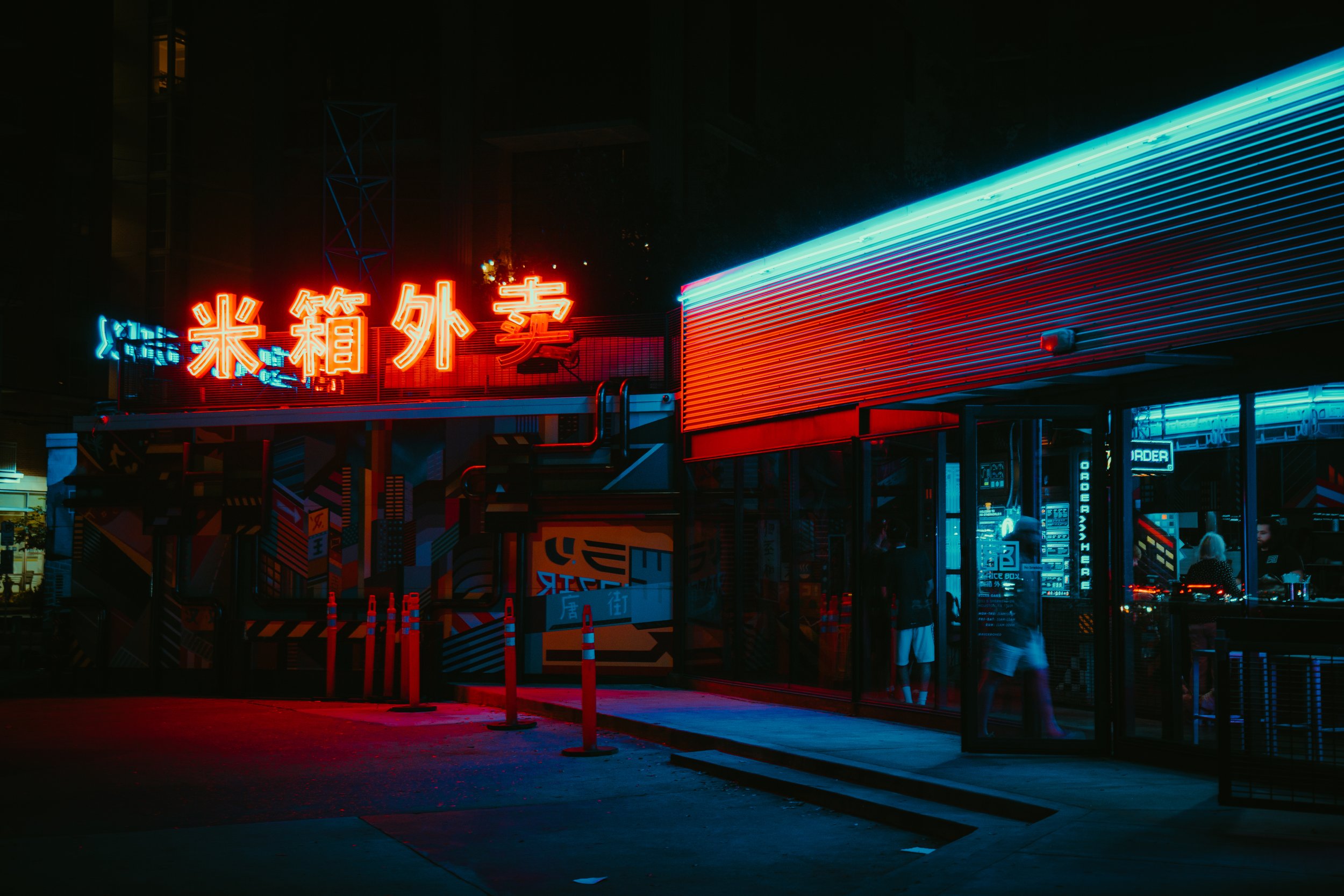 Nighttime neon-lit storefront with Chinese characters sign, colorful lights and a glass entrance with people inside