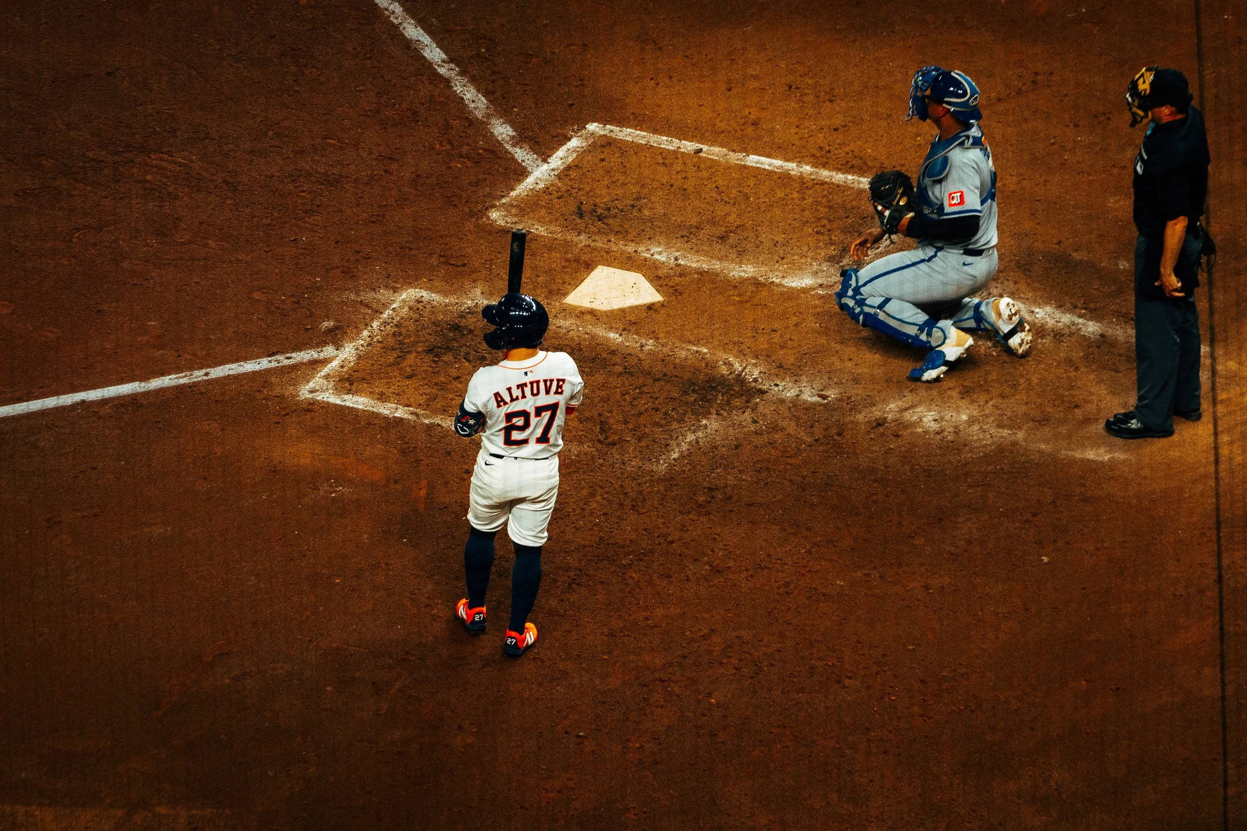 A baseball player at home plate with the name 'Altuve' and number 27, standing in a batting stance, facing the pitcher. A catcher is kneeling behind home plate, and an umpire is standing nearby on the dirt field.