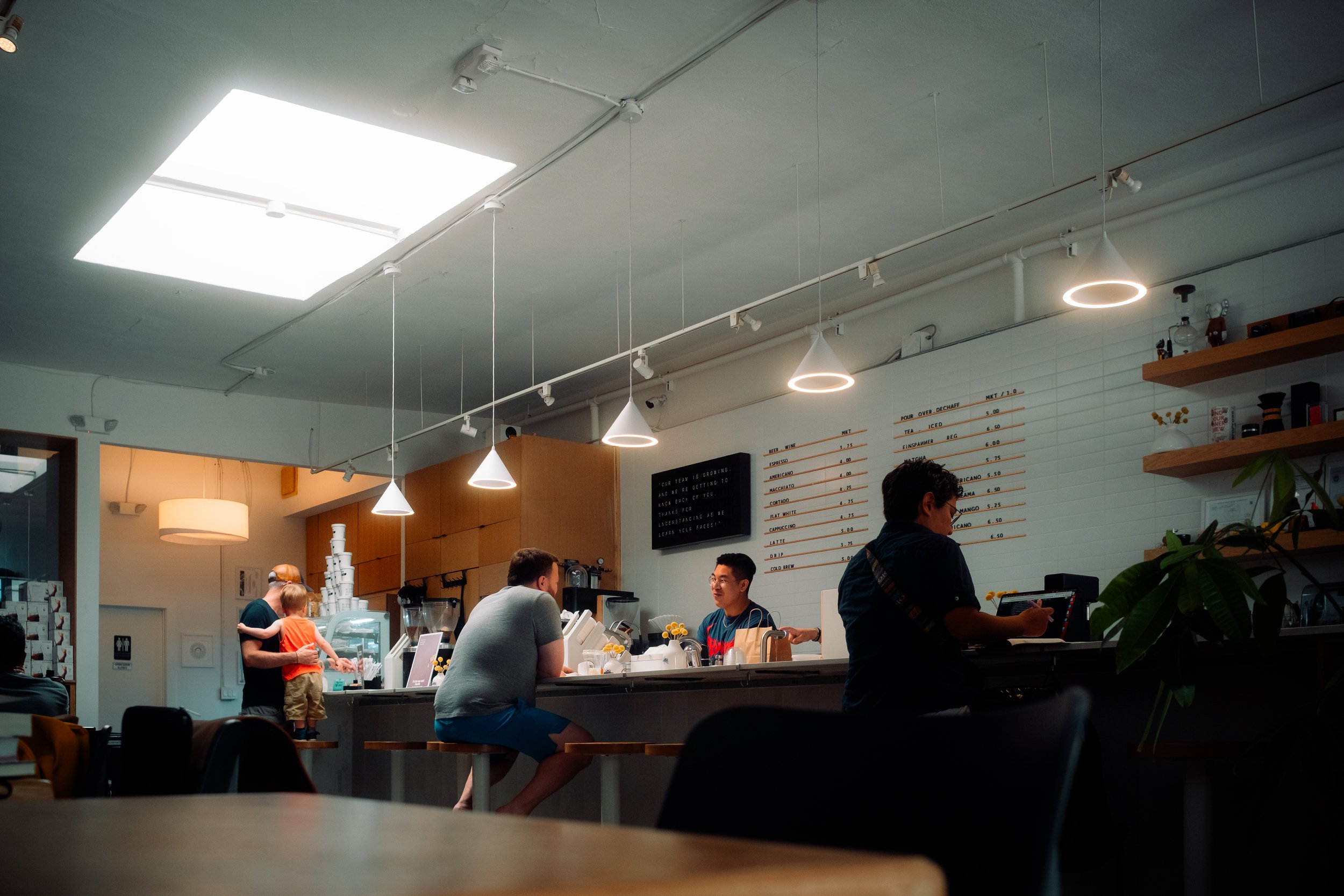 Interior of a modern coffee shop with customers at the counter and barista preparing orders.