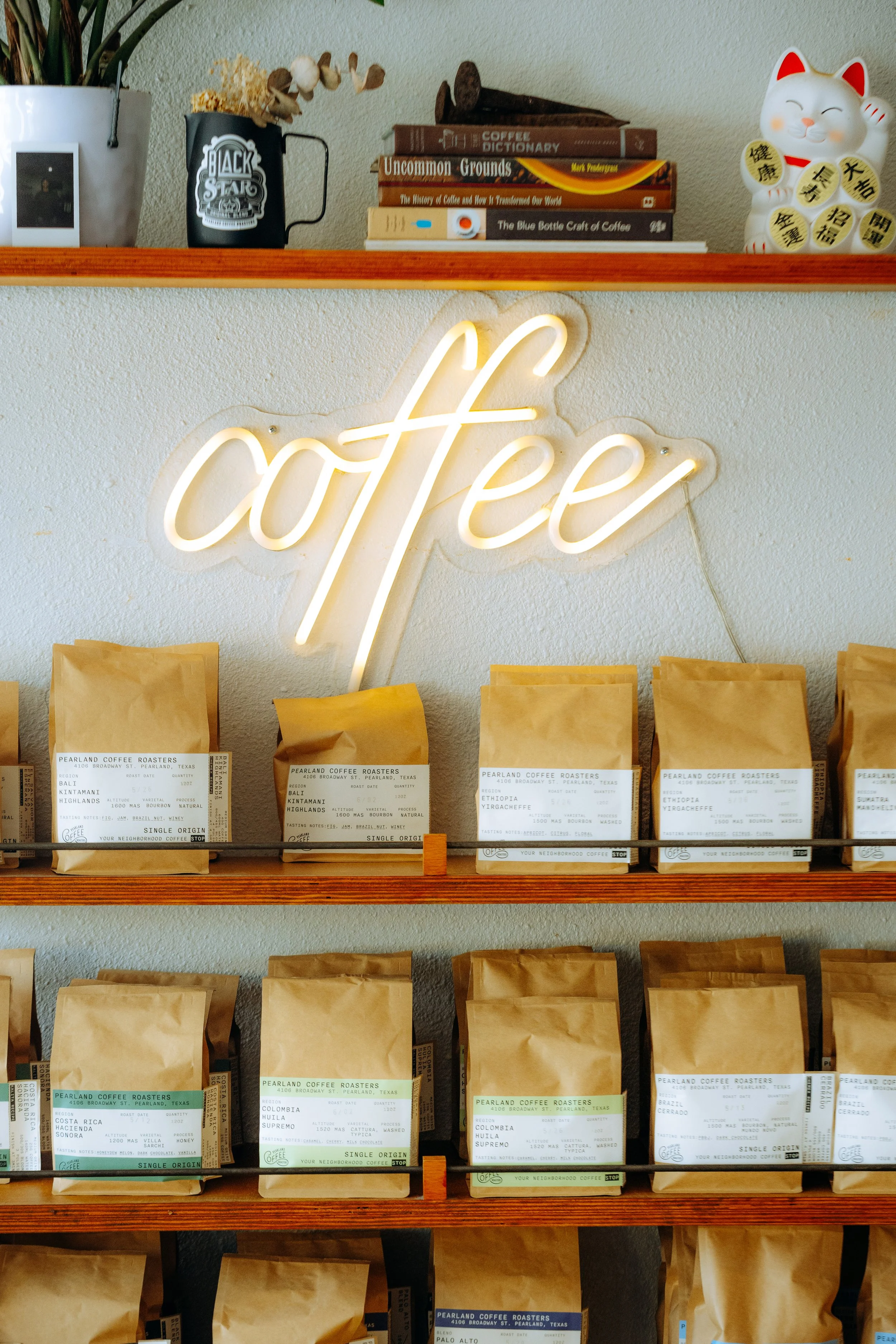 Neon sign that says 'coffee' above shelves of coffee bags in a coffee shop.