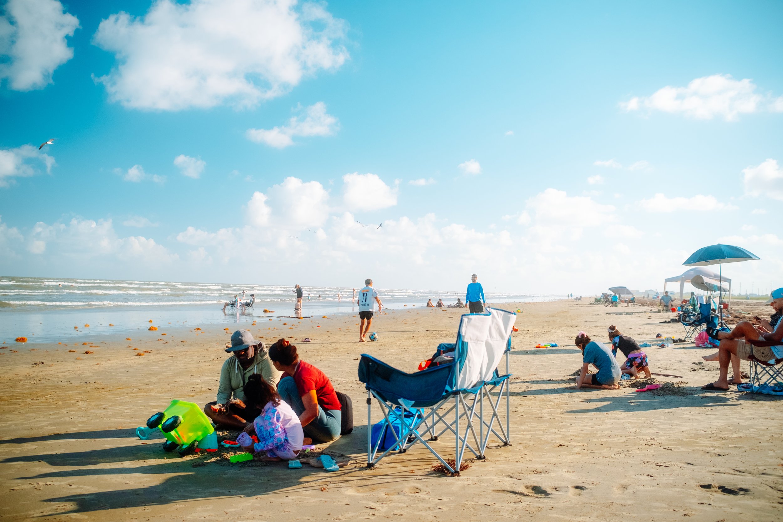 People enjoying a sunny day at the beach with umbrellas, chairs, and children playing in the sand.