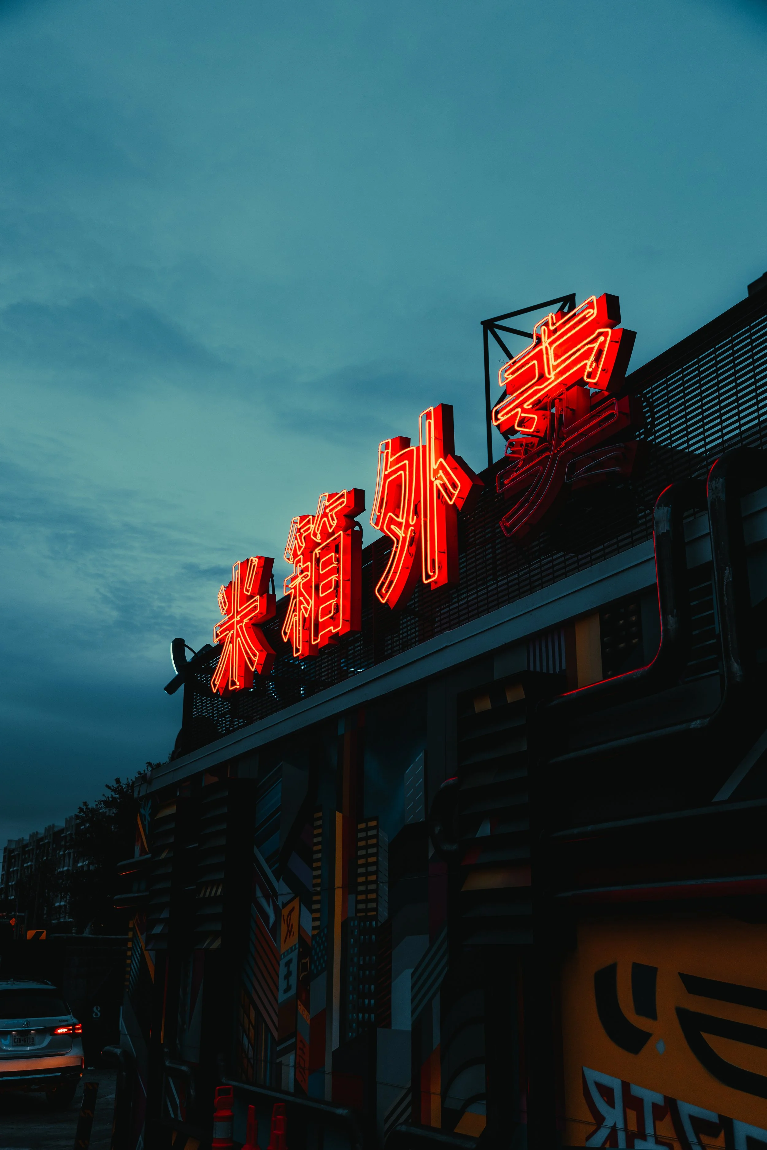 Neon red Chinese characters on a building against a cloudy sky.