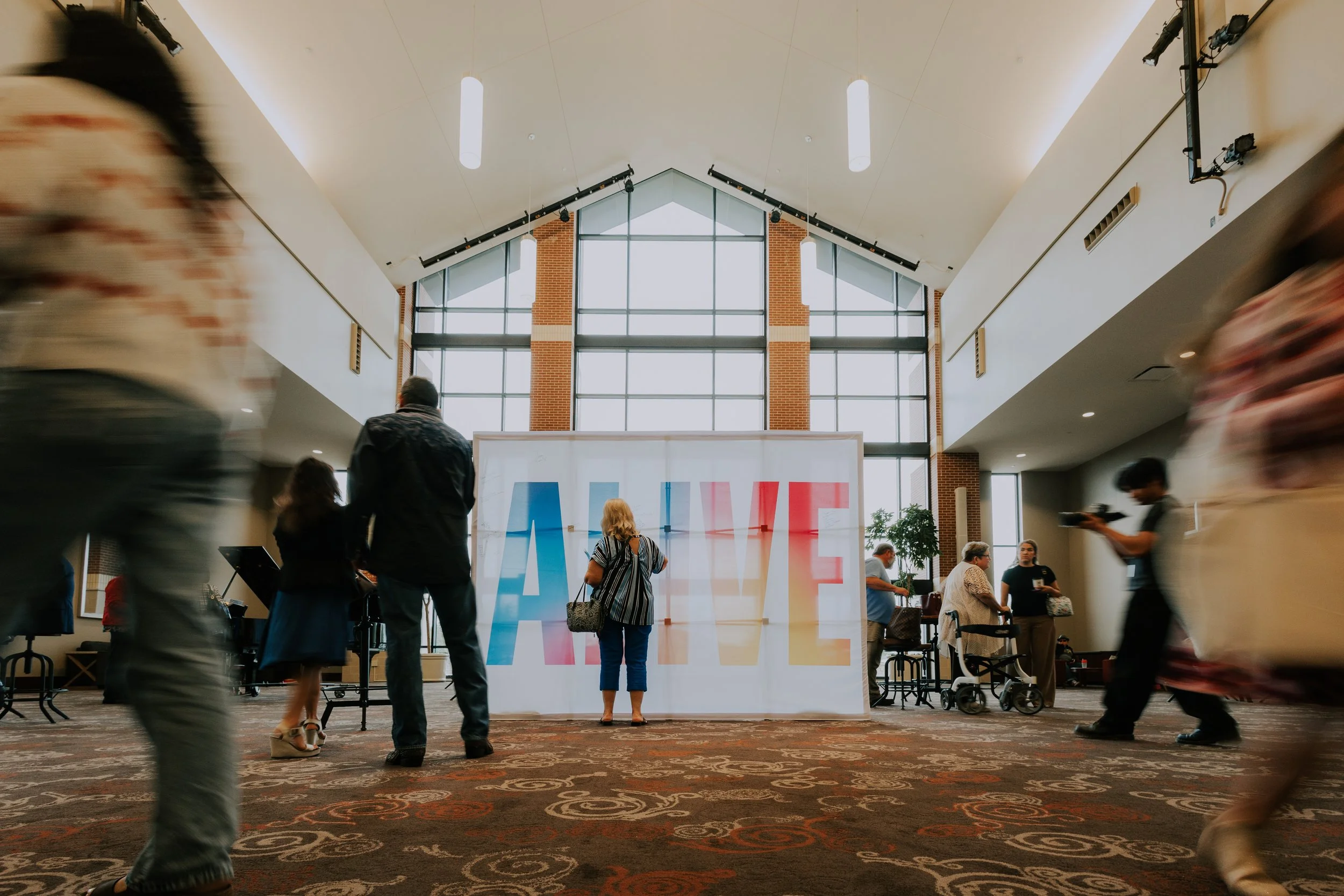 People in a spacious indoor lobby with a large colorful 'LOVE' sign and tall windows