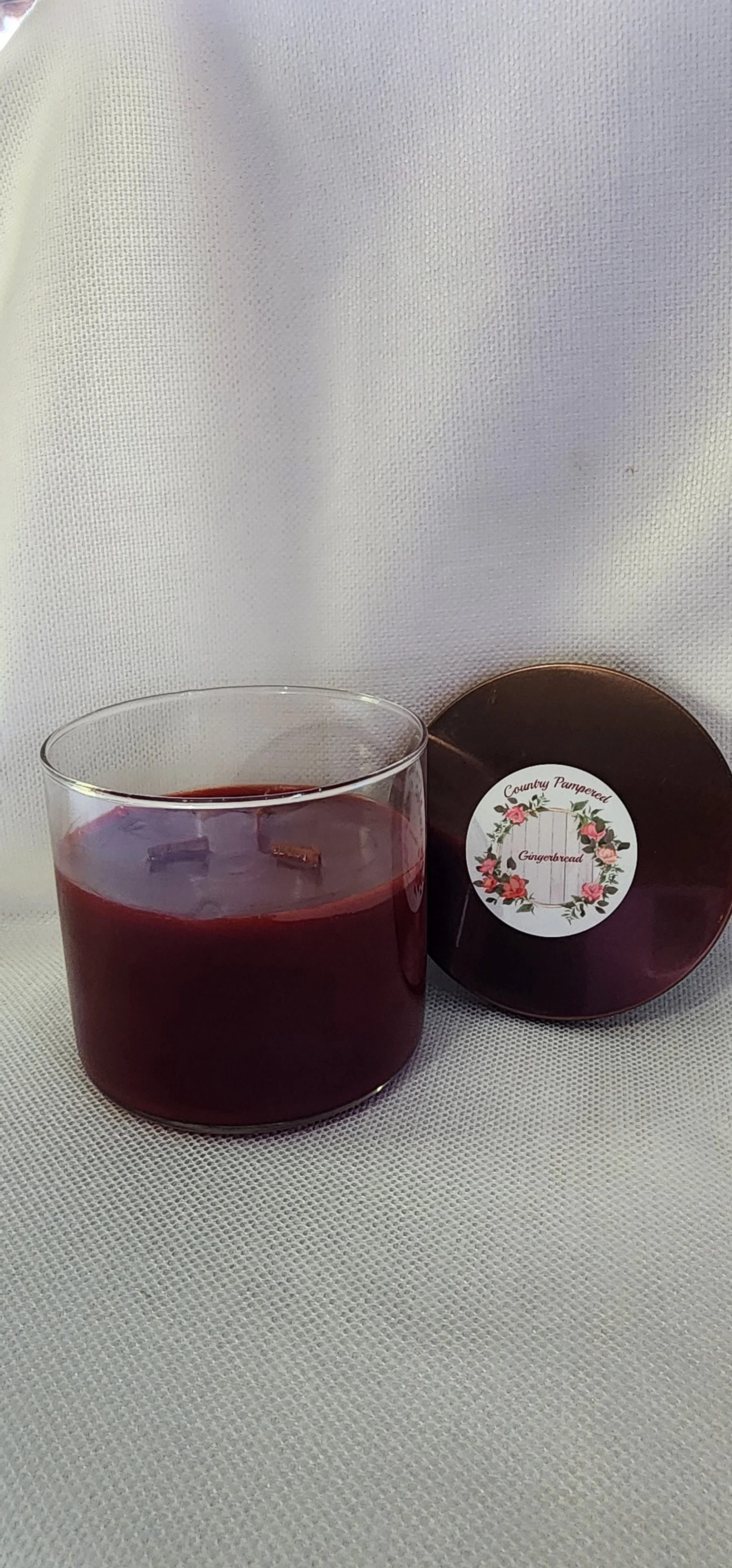 A glass jar of Gingerbread scented candle labeled 'Country Pampered' with a floral wreath design on the front, placed on a wooden surface.