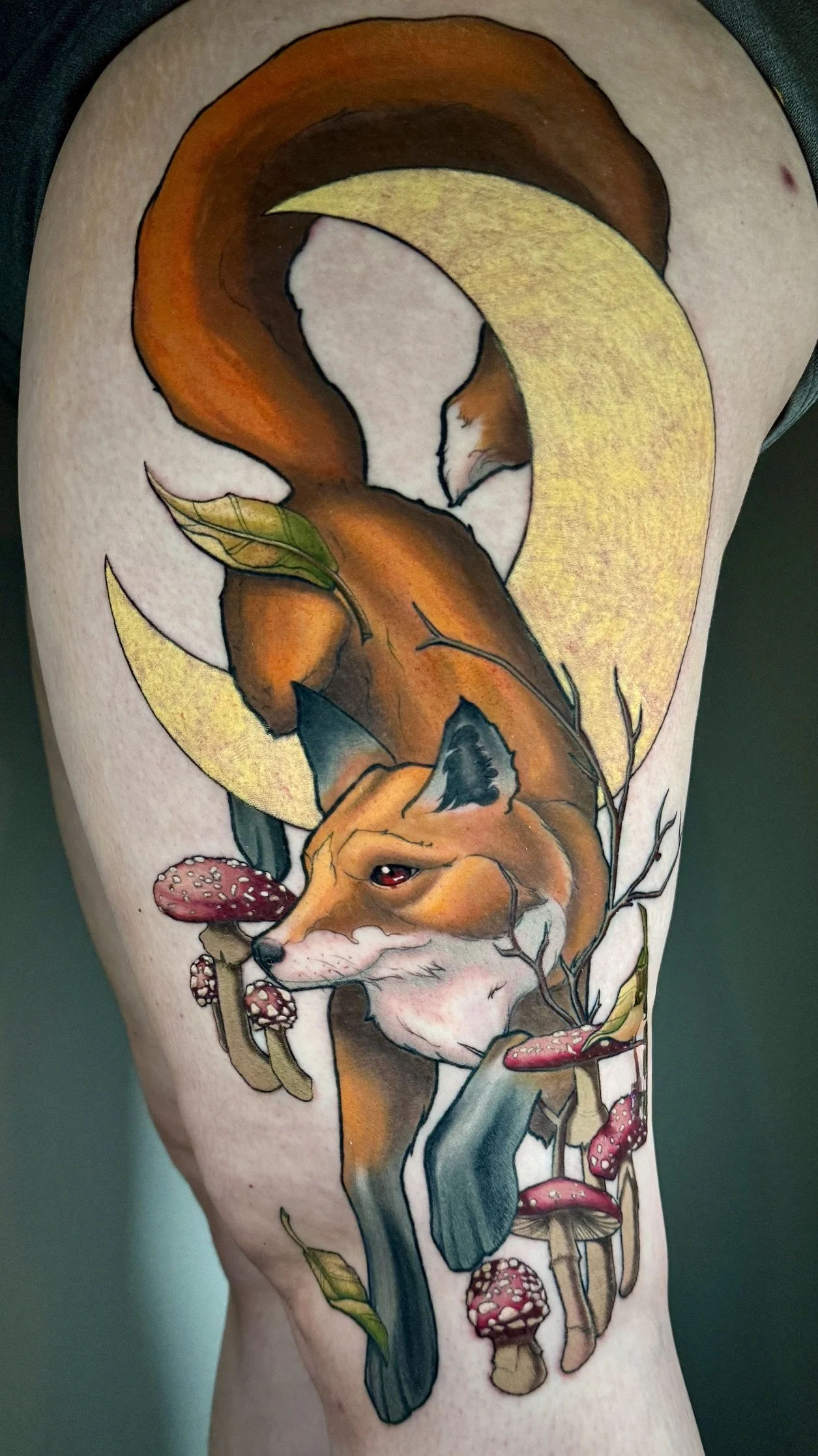 Tattoo of a fox curled around a crescent moon with mushrooms, leaves, and flowing water.