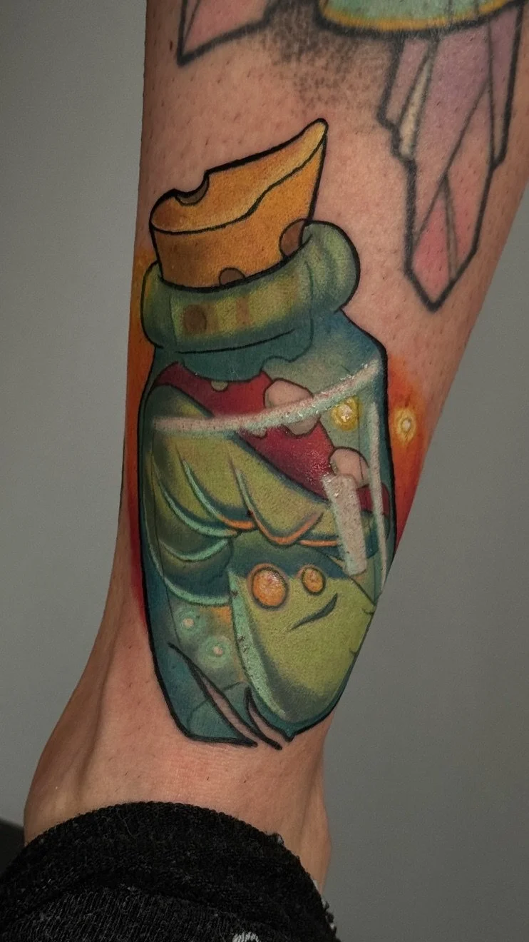 Colorful tattoo of a cartoon-style green heart with a bandage and small glowing yellow circles on a person's arm.