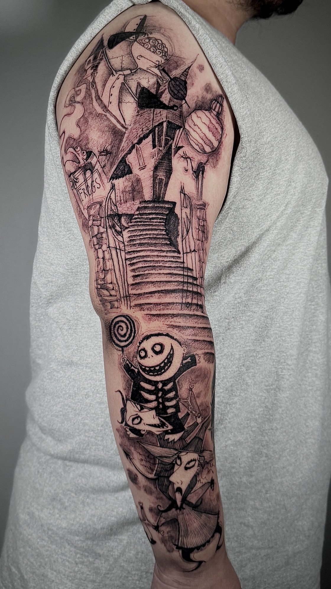 Tattoo sleeve featuring a staircase leading to a house, hot air balloons, a skeleton holding a lollipop, and various whimsical characters.