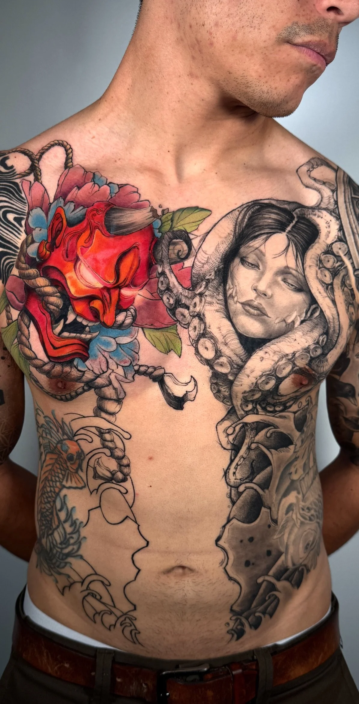 A man with a detailed chest tattoo featuring a woman’s face wrapped by an octopus, colorful flowers, and other elements.