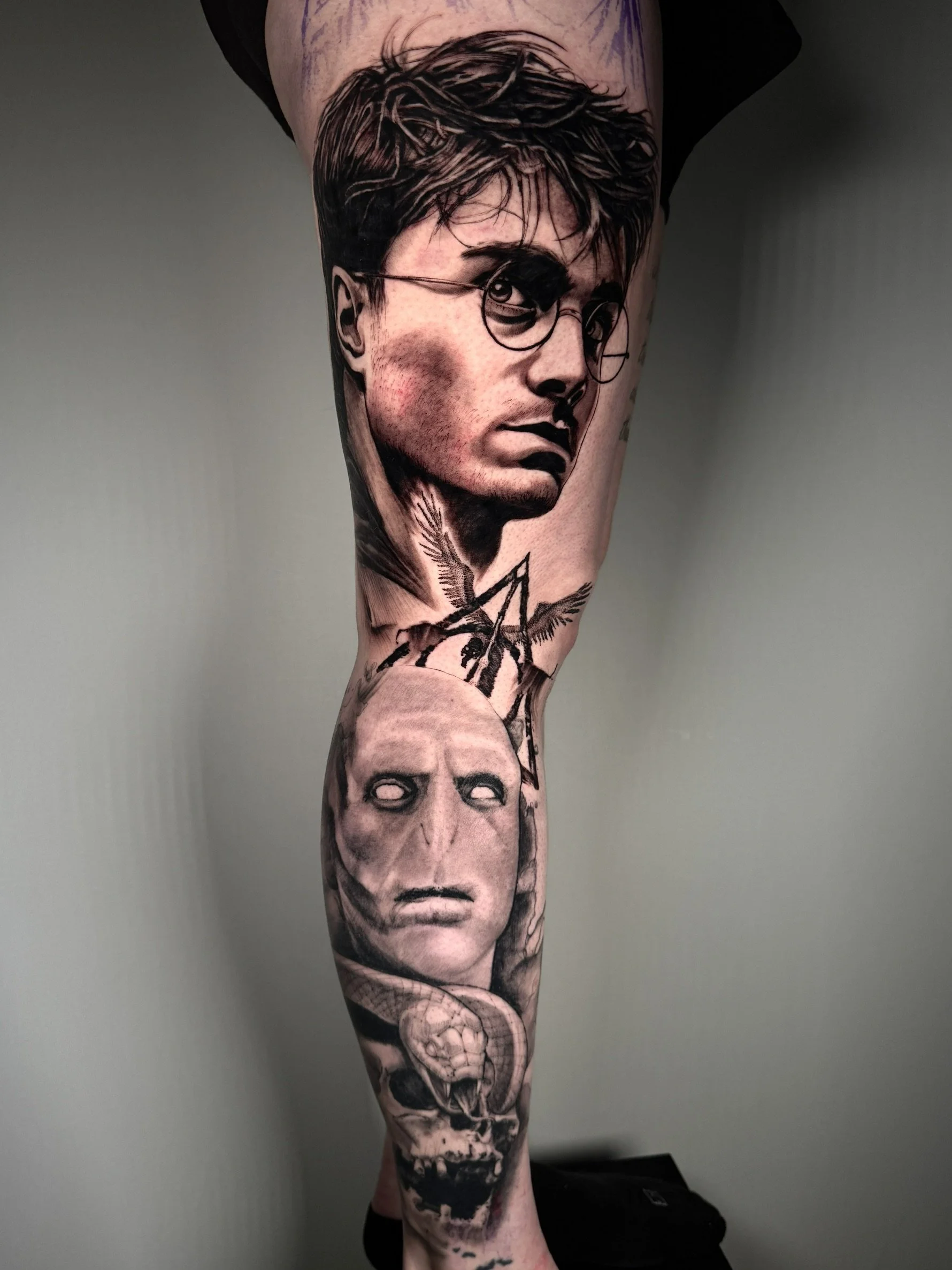 Tattoo sleeve featuring multiple faces, including a prominent portrait of a young man with glasses, with various other illustrations of faces and skulls below.