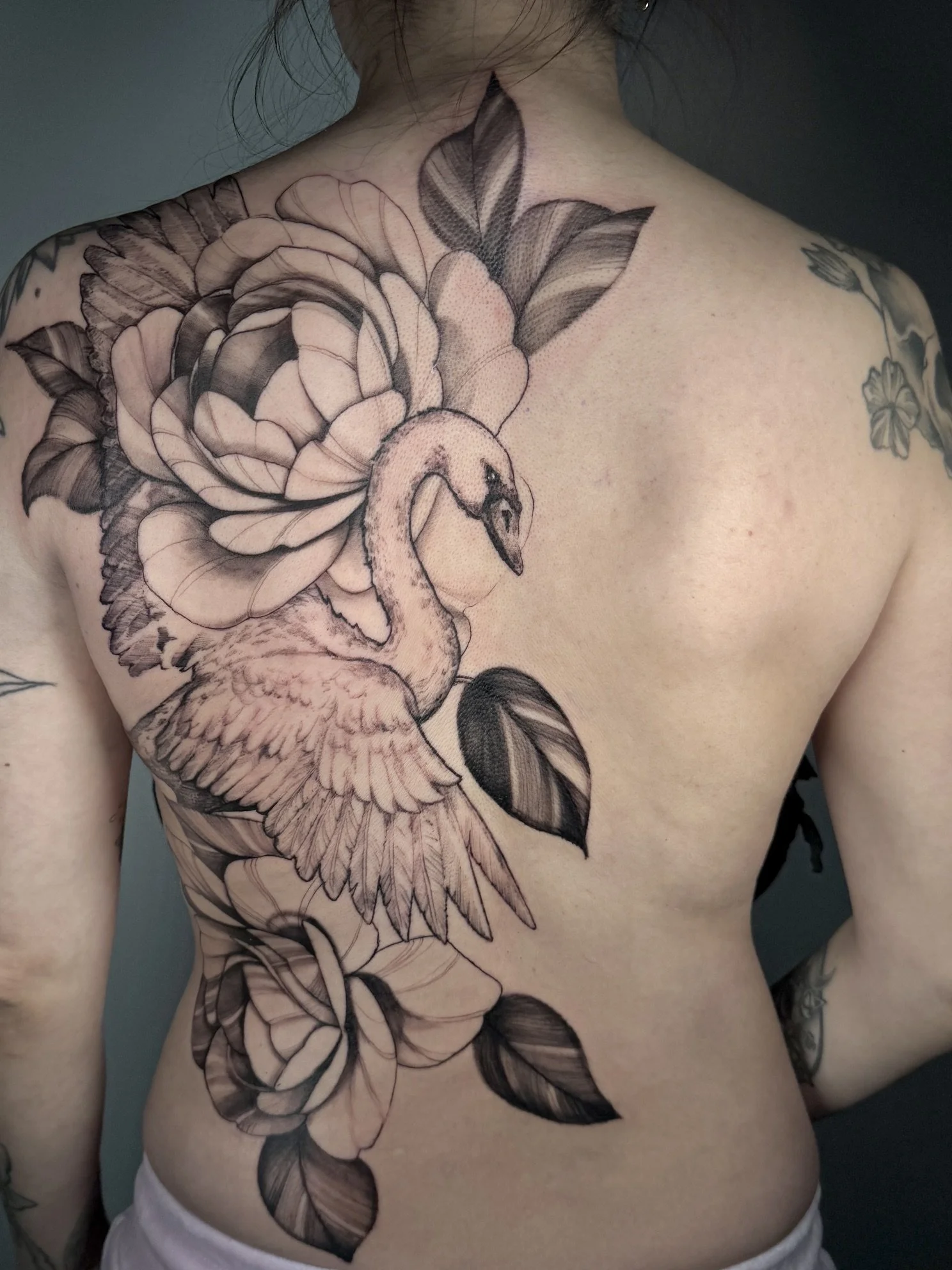 Black and gray floral tattoo of a swan and peony on person's chest and shoulder.