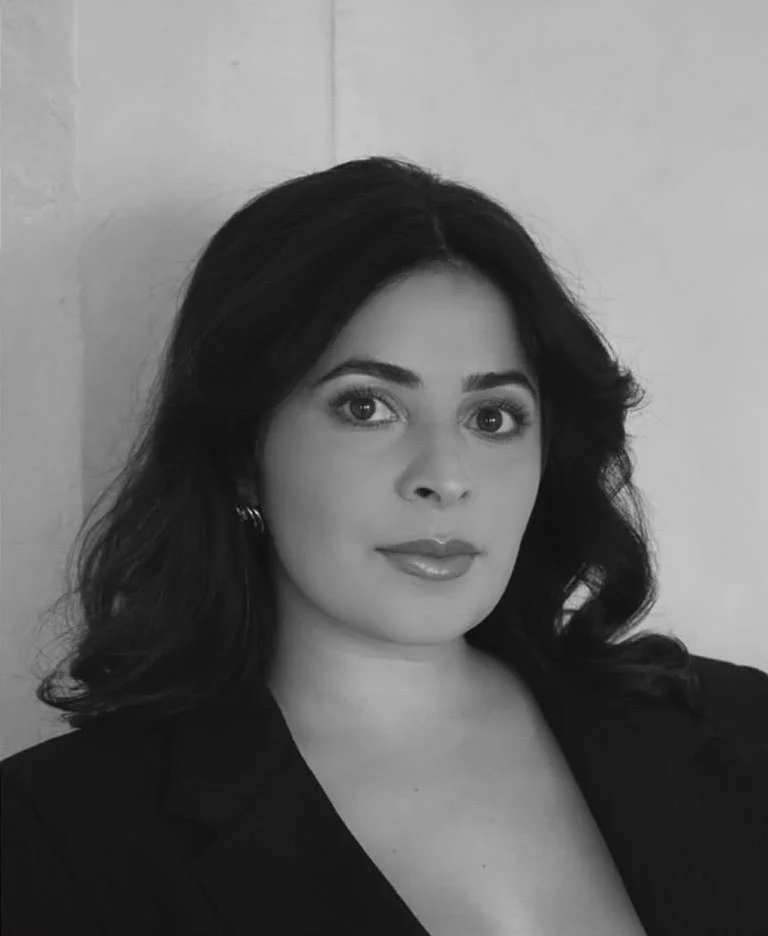 Black and white portrait of a woman with dark hair, wearing earrings and a blazer, looking directly at the camera.